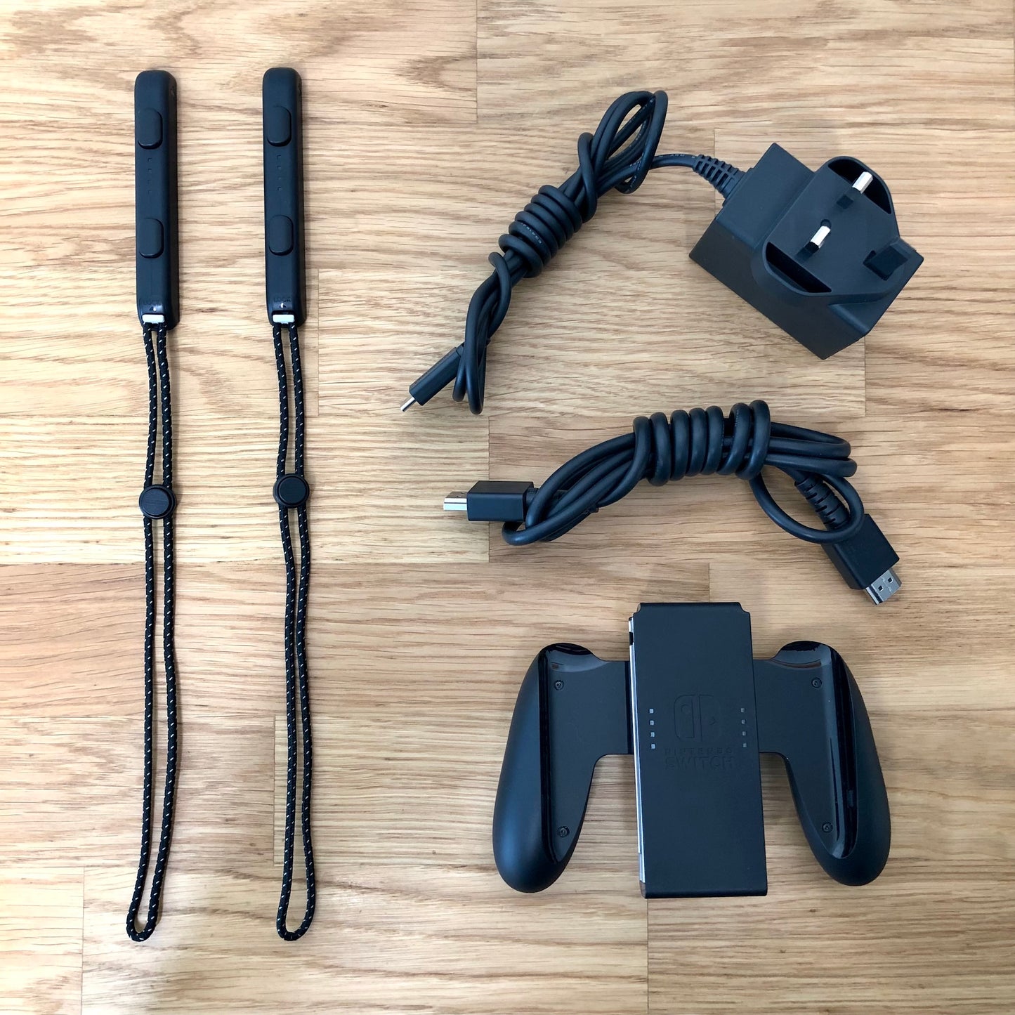 Nintendo Switch OLED accessories including Joy-Con straps, HDMI cable, charger plug and Joy-Con grip laid out.