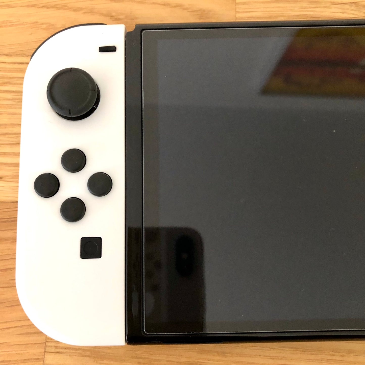 Close-up of white left Joy-Con on Nintendo Switch OLED, showing D-pad style buttons, left stick and minus button.