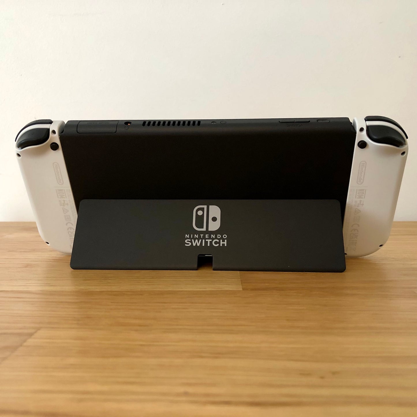 Back of Nintendo Switch OLED with kickstand open, showing logo, game card slot, vent and volume controls.