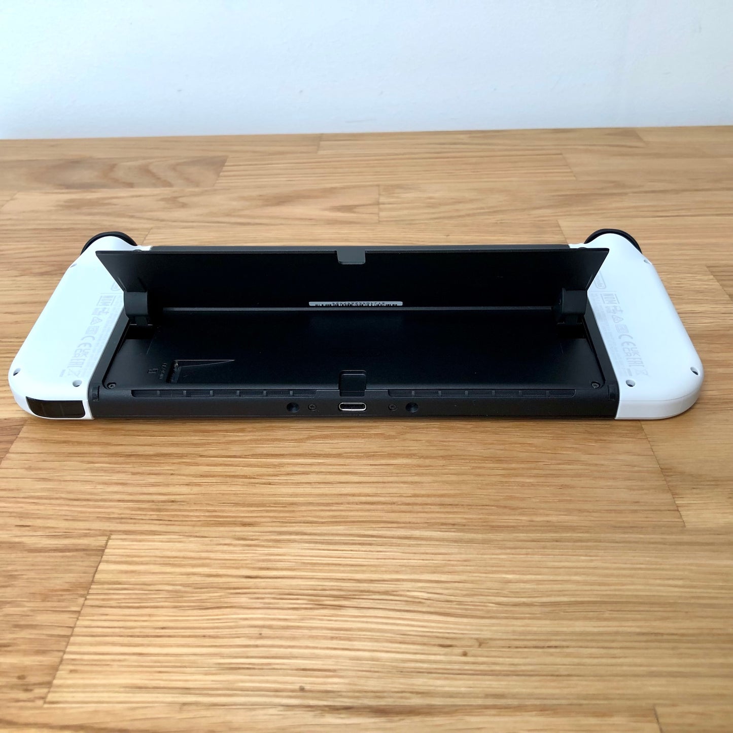 Bottom rear view of Nintendo Switch OLED with kickstand lifted, showing microSD slot, USB-C port and controls.
