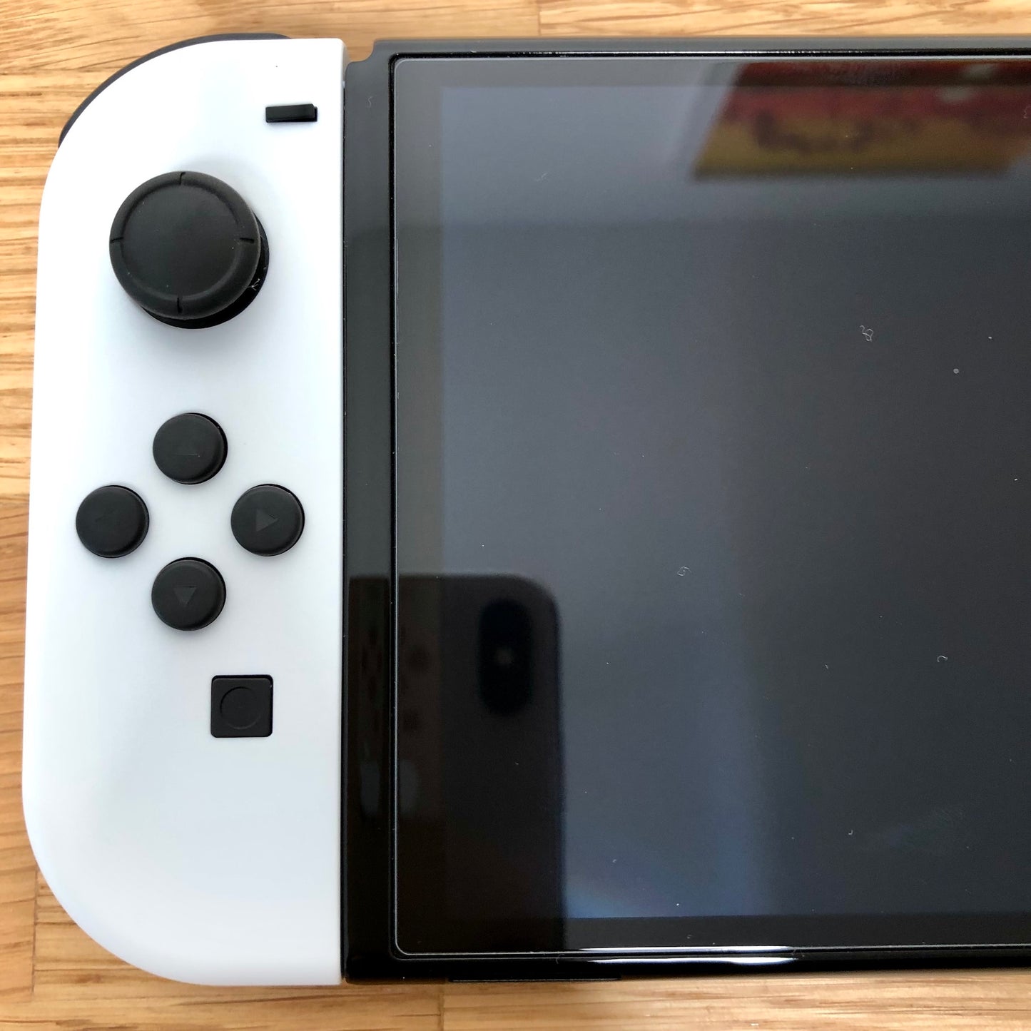 Close-up of white left Joy-Con on Nintendo Switch OLED, showing D-pad style buttons, left stick and minus button.