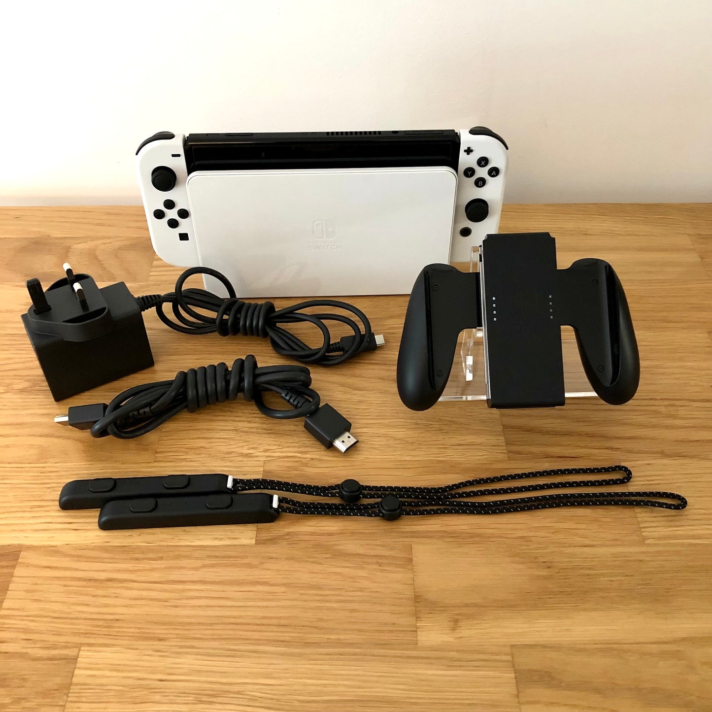 White Nintendo Switch OLED console with charger, HDMI cable, Joy-Con grip and wrist straps laid out.