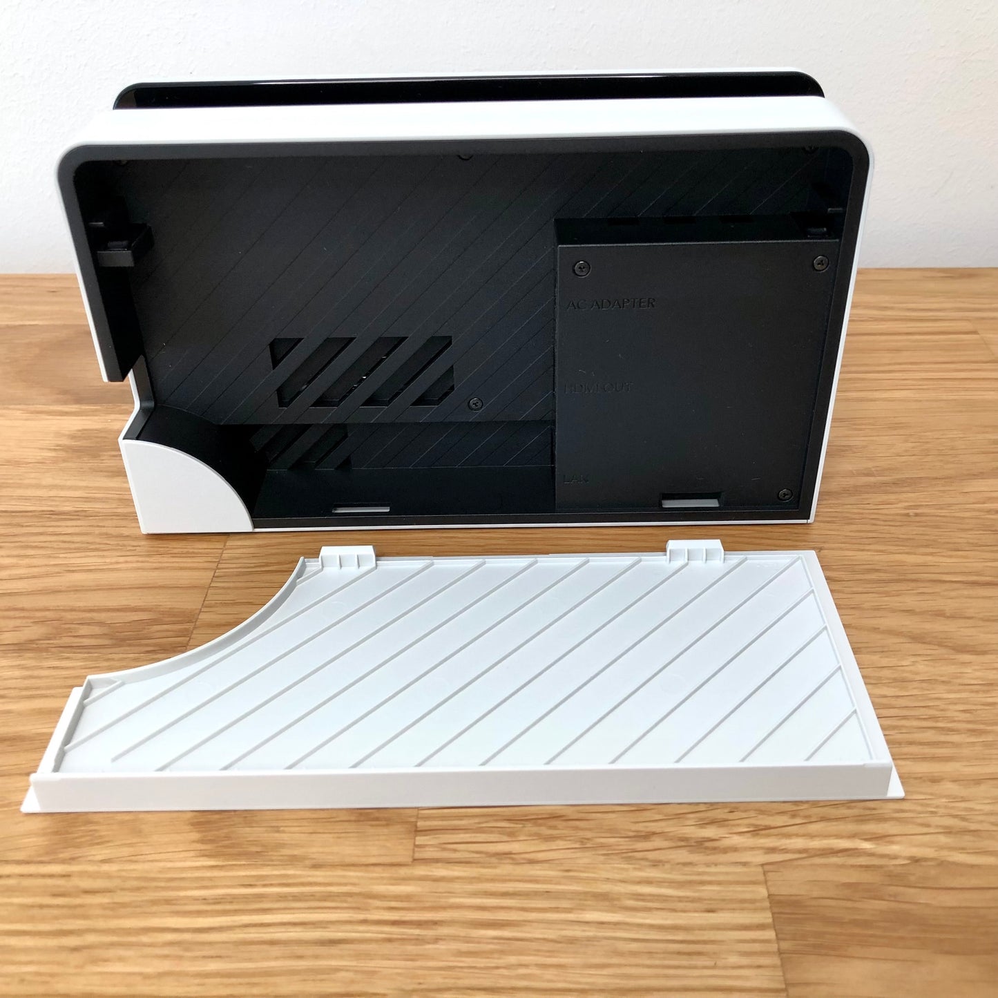 Inside of white Nintendo Switch OLED dock with flap open, showing ports for AC adapter, HDMI out and LAN.