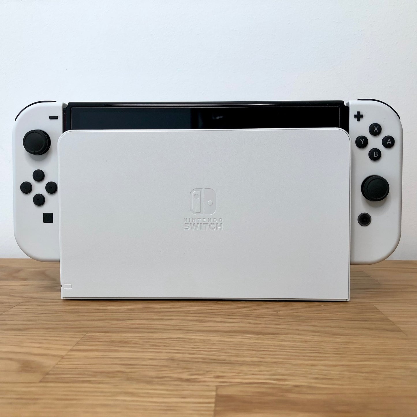 Front of Nintendo Switch OLED console docked, showing white Joy-Cons with button layout visible on both sides.