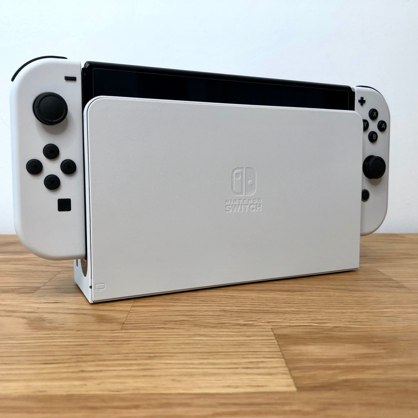 Angled view of Nintendo Switch OLED console docked, showing white Joy-Cons with visible buttons and sticks.