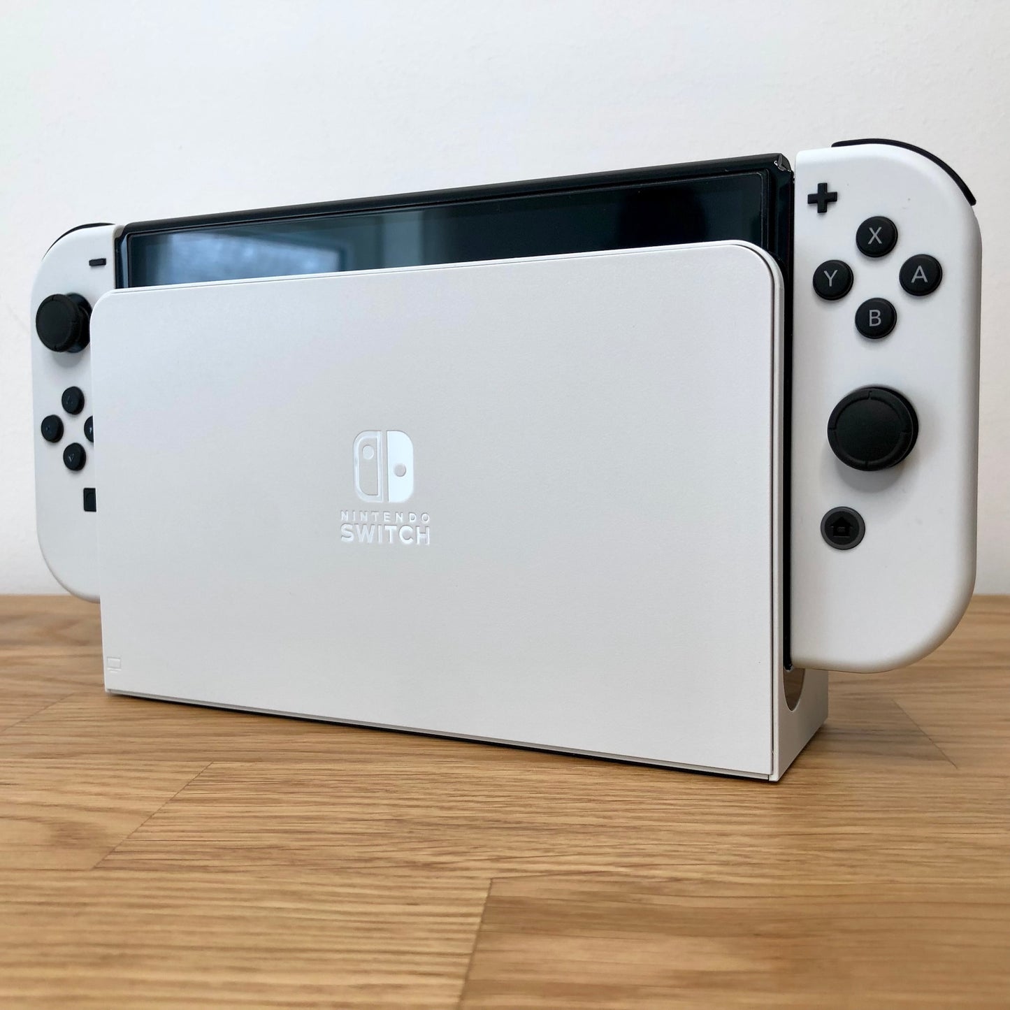 Angled view of Nintendo Switch OLED console docked, showing white Joy-Cons with visible buttons and sticks.