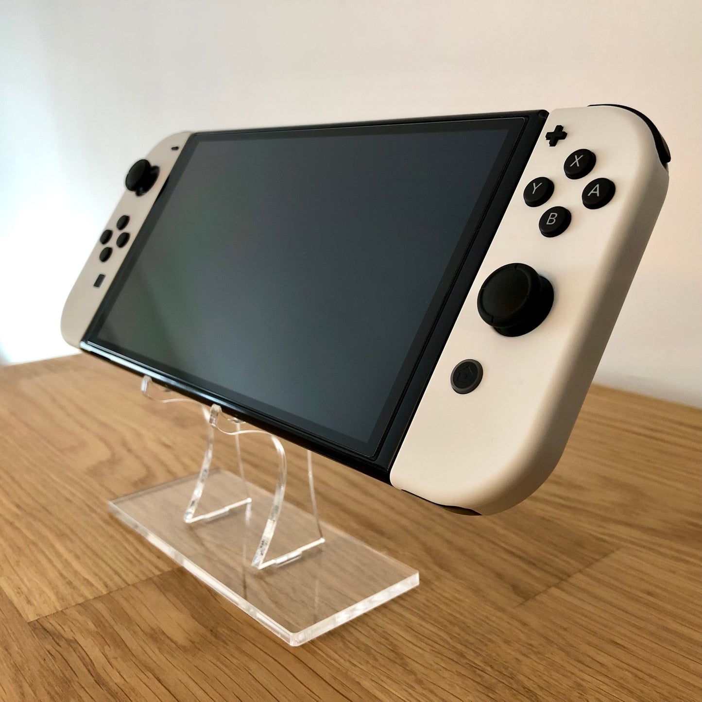 Angled front of Nintendo Switch OLED with white Joy-Cons, showing full face buttons, control sticks and screen.