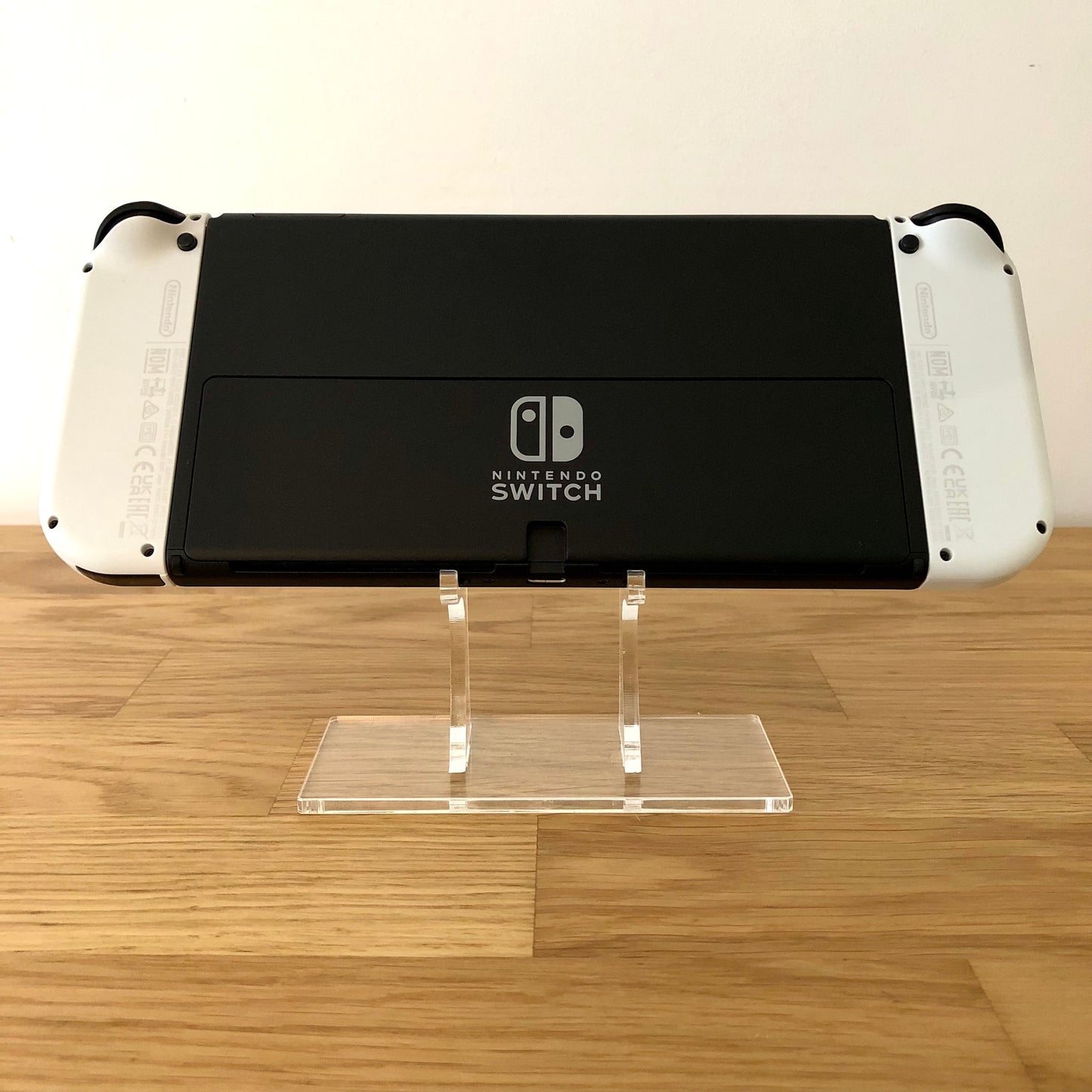 Back of Nintendo Switch OLED console with white Joy-Cons attached, showing logo, kickstand and trigger buttons.