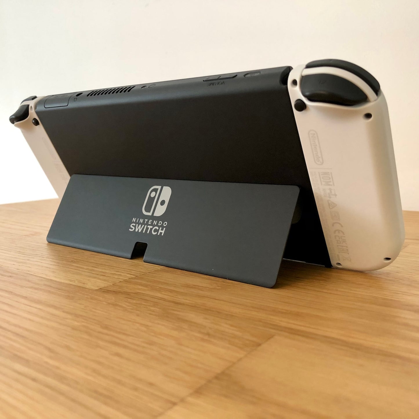 Angled rear view of Nintendo Switch OLED with kickstand open, showing logo, triggers and top-side buttons.