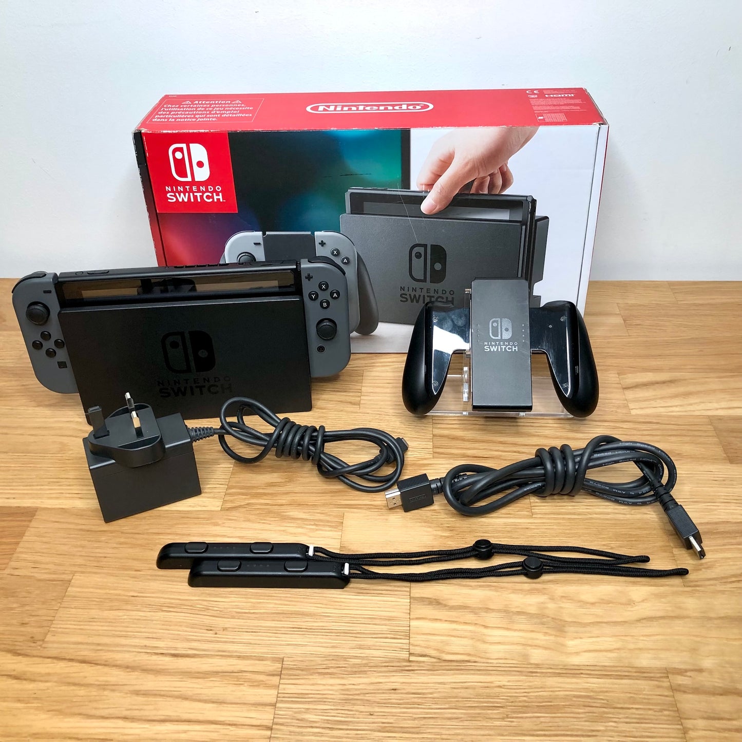 Grey Nintendo Switch console with original box, Joy-Con grip, charger, HDMI cable and wrist straps shown.