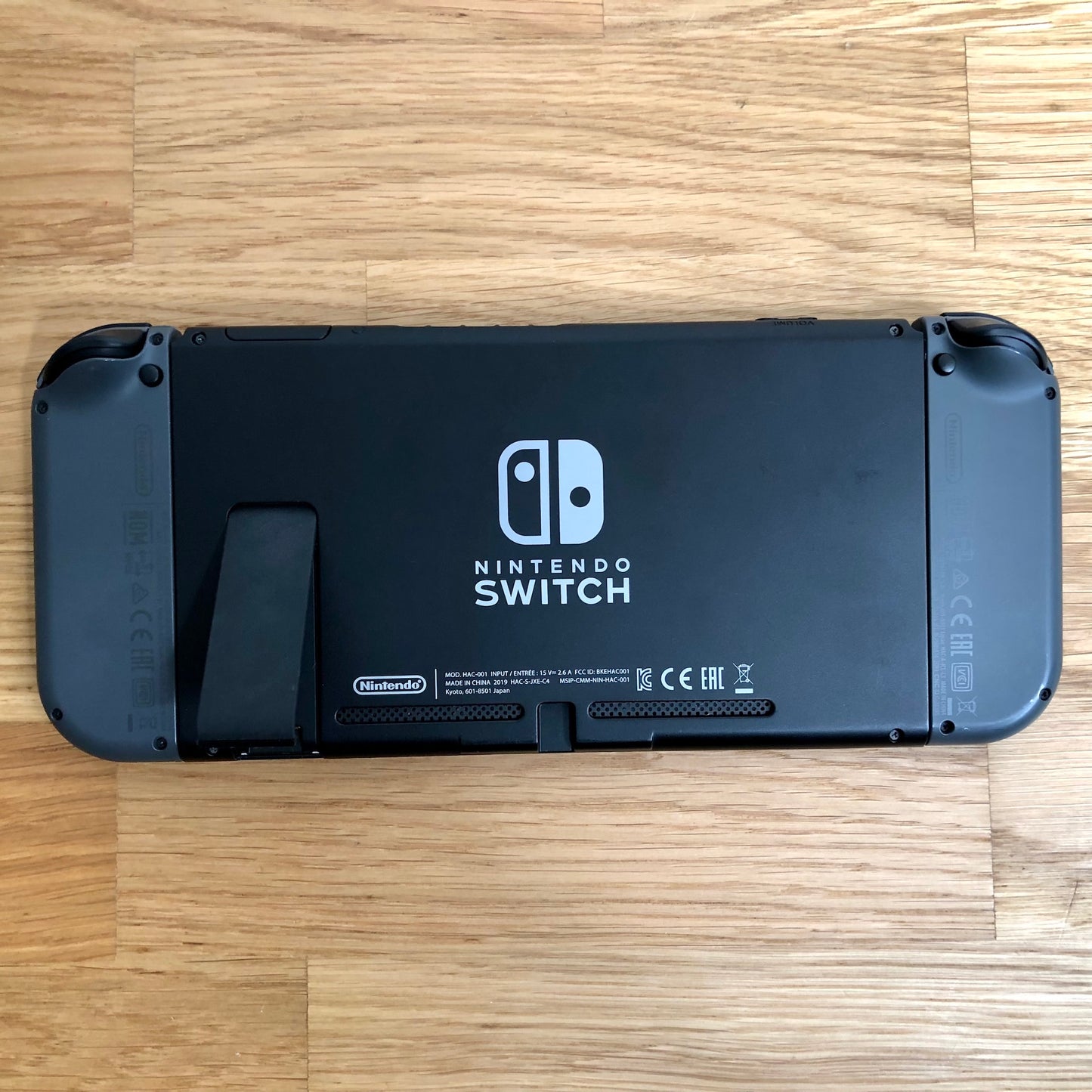 Back of Nintendo Switch console laying flat with grey Joy-Cons attached, showing logo, kickstand and trigger buttons.