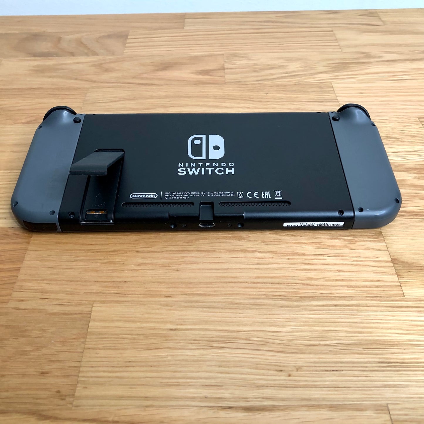 Bottom rear view of Nintendo Switch with grey Joy-Cons attached, showing logo, kickstand and microSD slot.