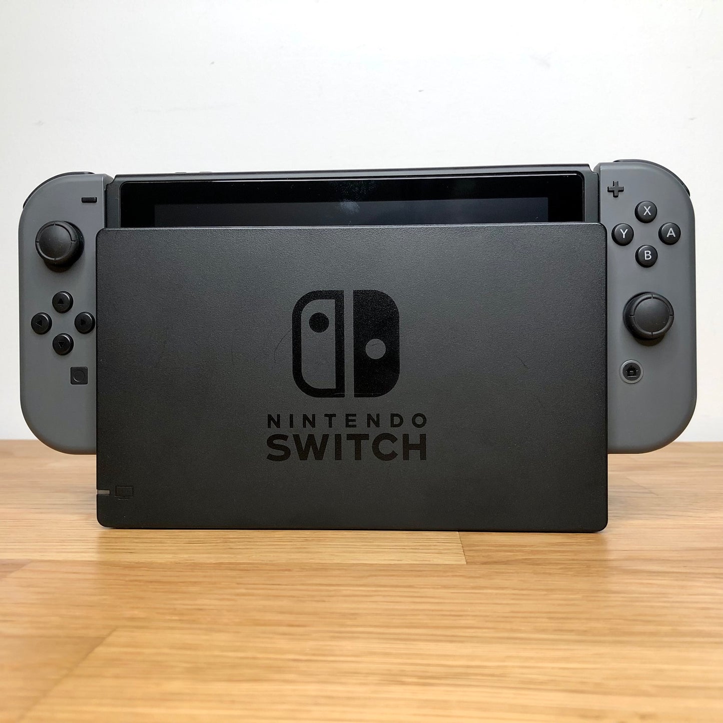Front of grey Nintendo Switch console docked, showing Joy-Cons with all face buttons and screen edge visible.