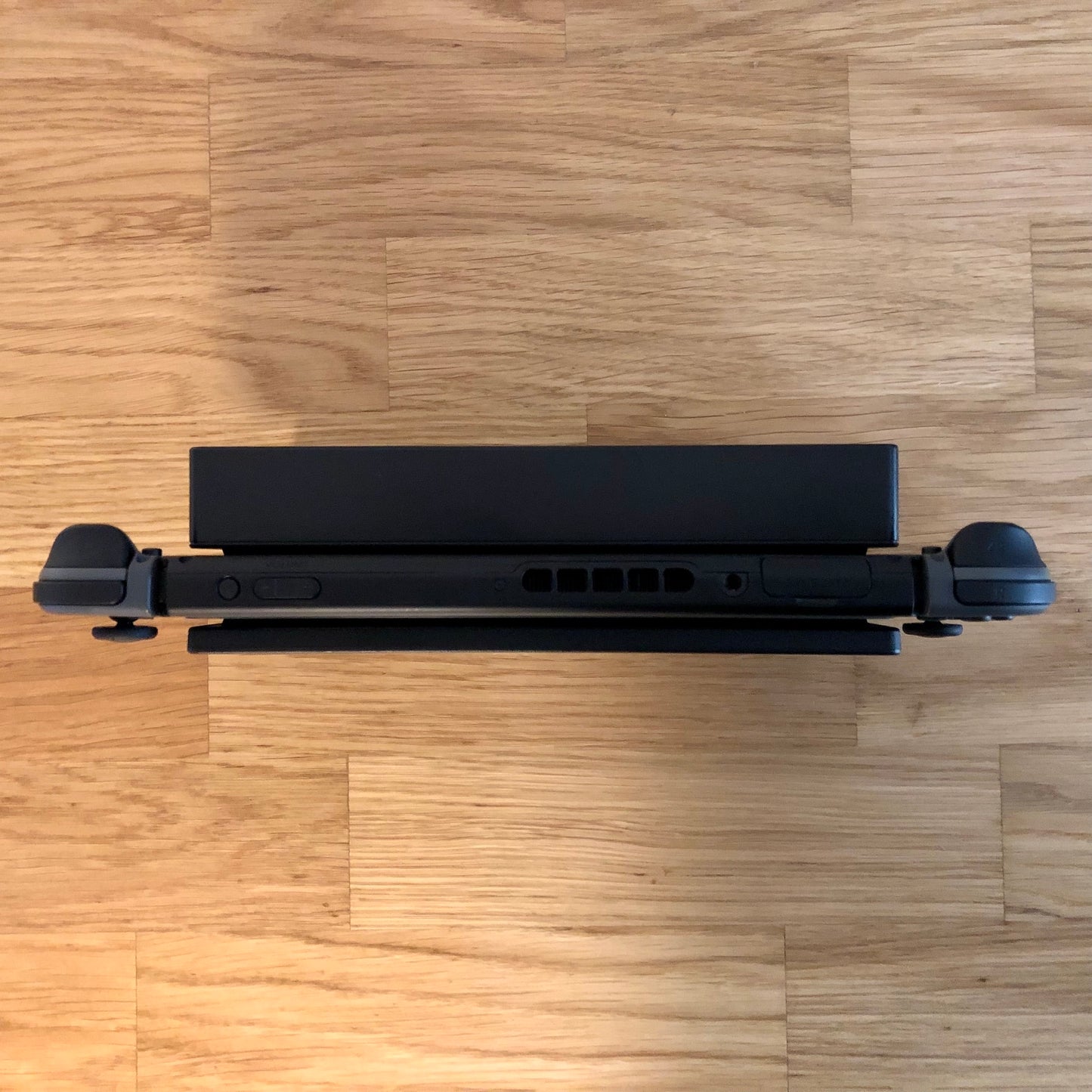 Top-down view of grey Nintendo Switch in dock, showing triggers, volume, power and game card slot.