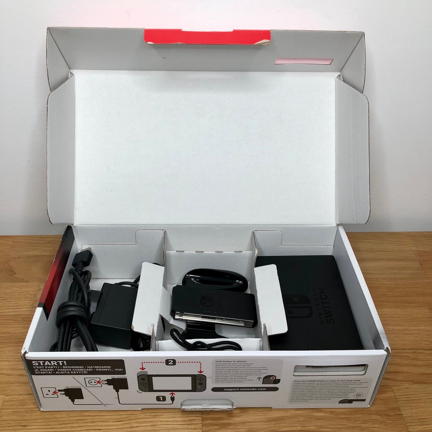 Second layer of Nintendo Switch box showing dock, Joy-Con grip, HDMI cable, charger and straps securely packed.