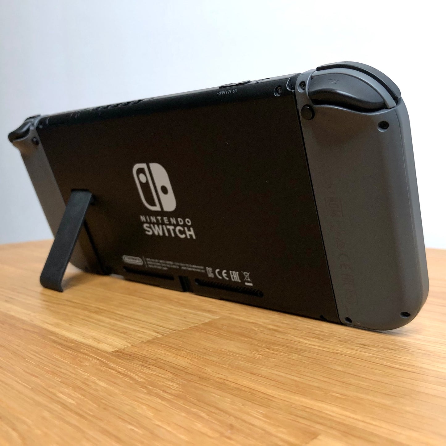 Back angled view of Nintendo Switch console with grey Joy-Cons attached, showing logo, kickstand and trigger buttons.