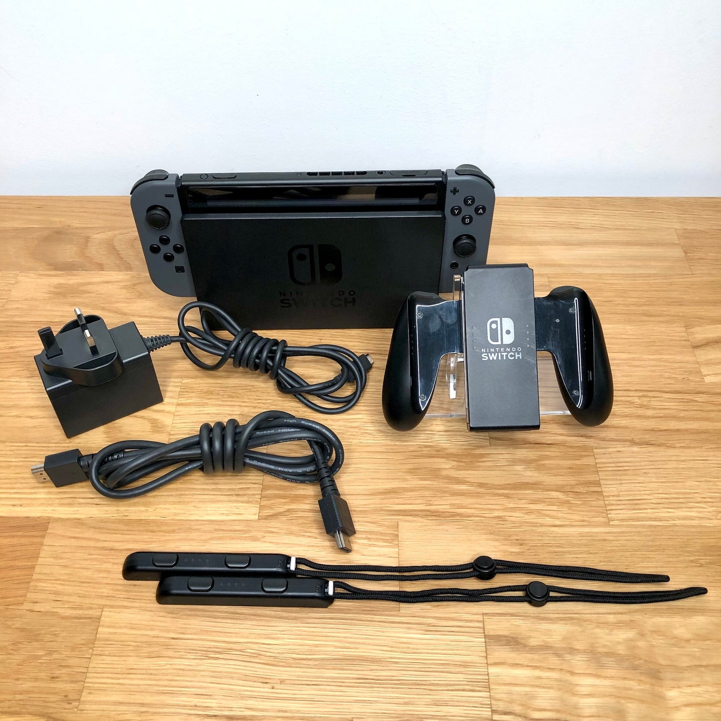 Grey Nintendo Switch console with original box, Joy-Con grip, charger, HDMI cable and wrist straps shown.
