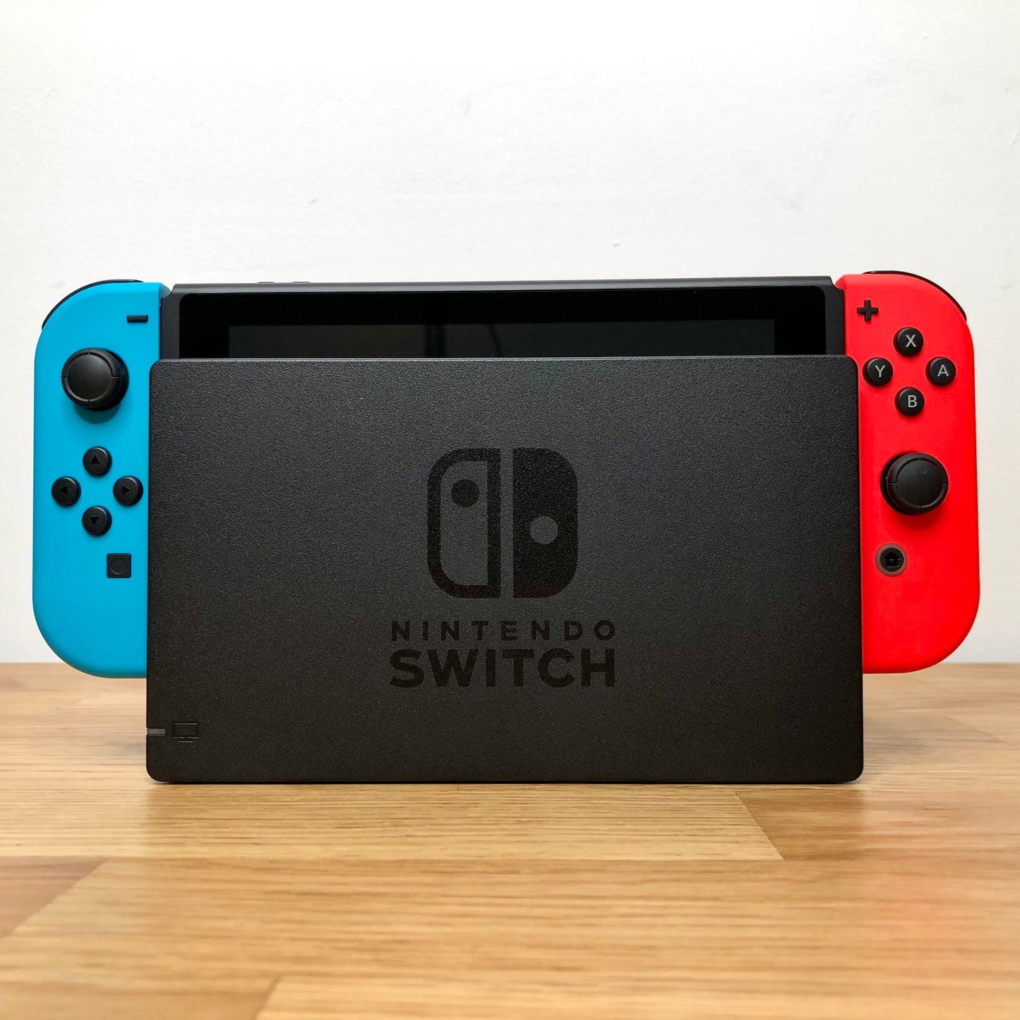 Front of Nintendo Switch console docked with red and blue Joy-Cons, showing screen edge and front buttons.