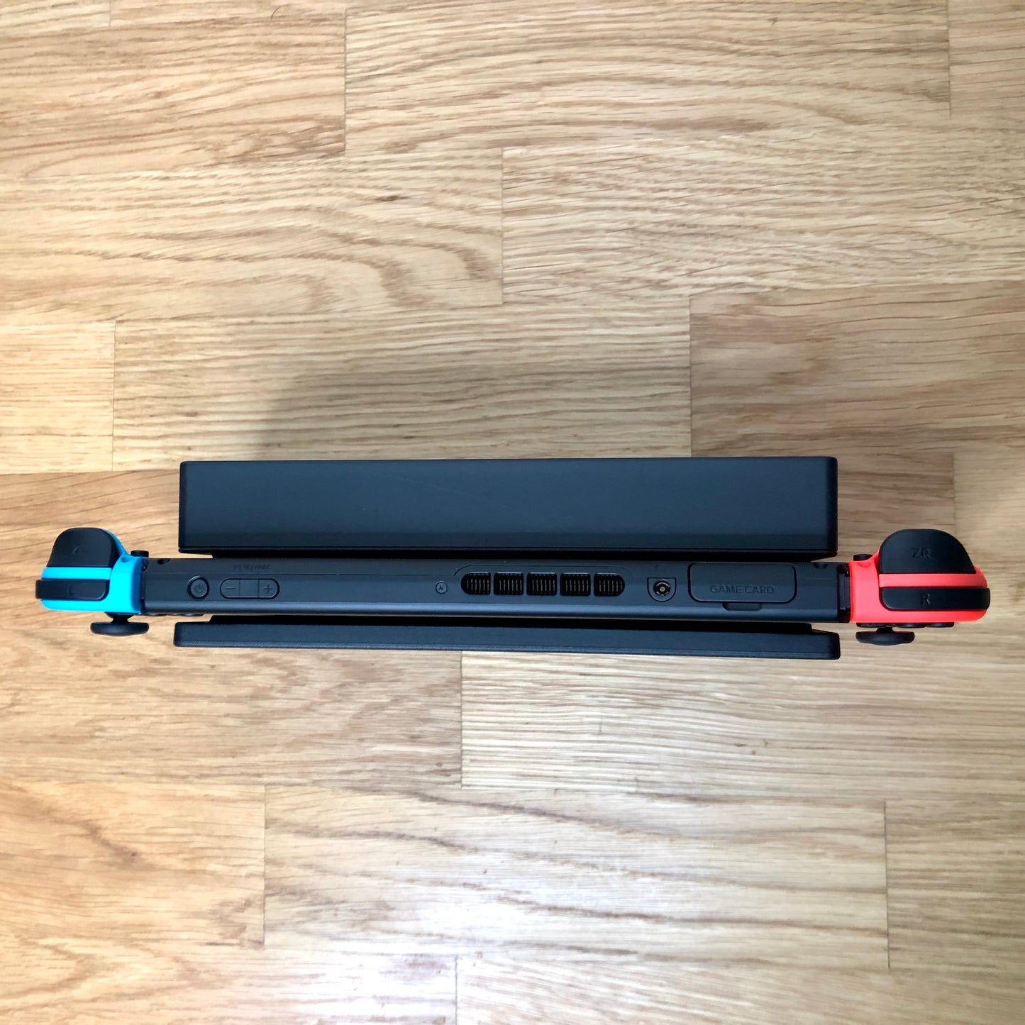 Top-down view of Nintendo Switch in dock with red and blue Joy-Cons, showing triggers, game card slot and volume buttons.