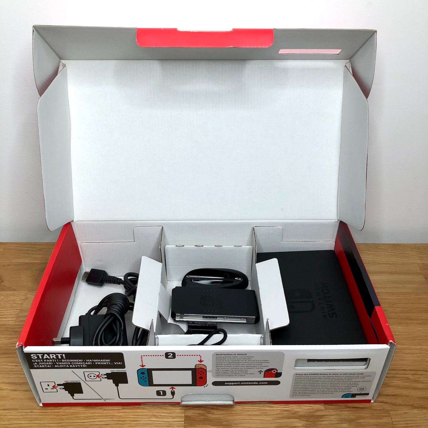 Second layer of Nintendo Switch box showing dock, Joy-Con grip, HDMI cable, charger and straps securely packed.