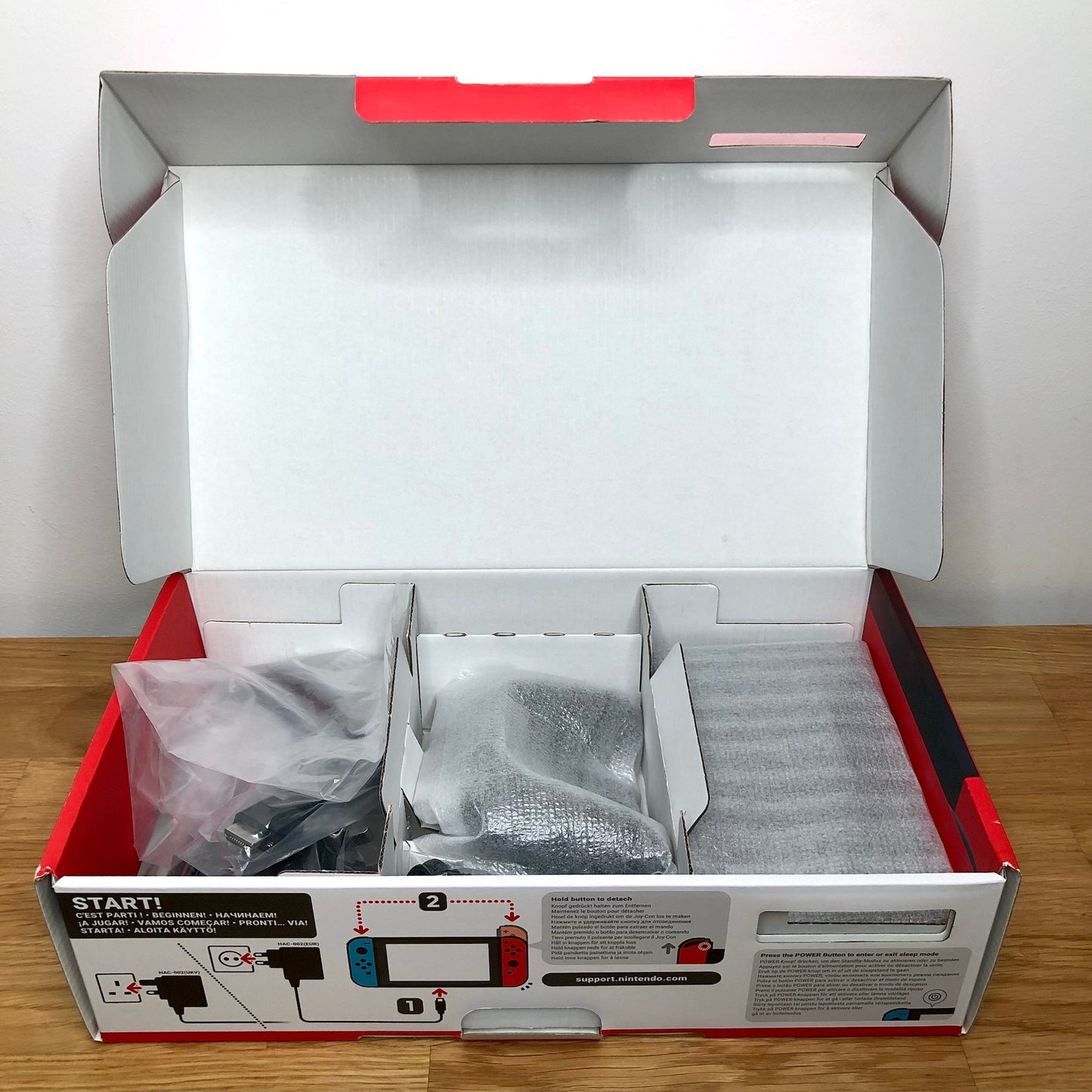 Second layer of Nintendo Switch box showing dock, Joy-Con grip, HDMI cable, charger and straps securely packed.