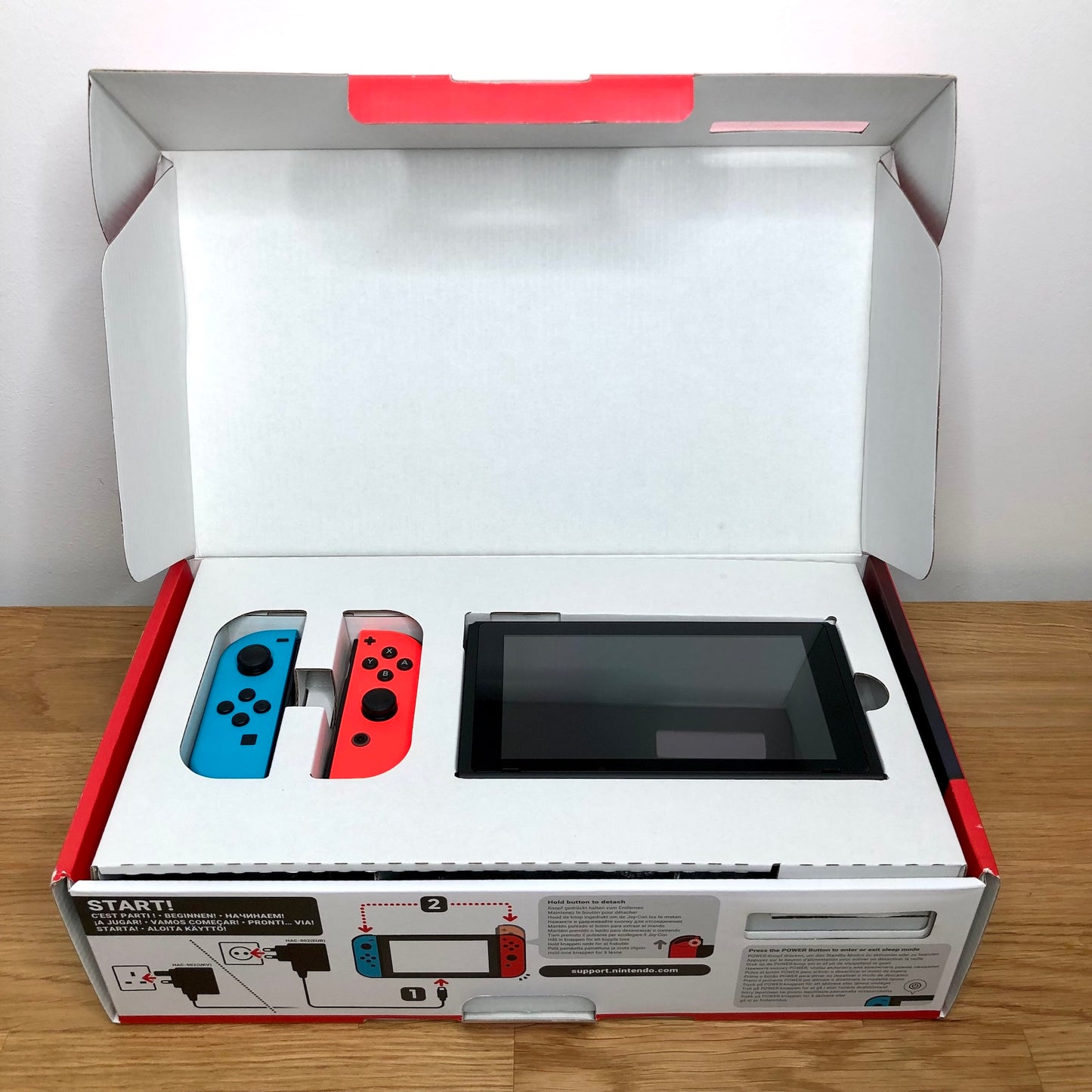 Nintendo Switch console in original box with lid open, showing console and red and blue Joy-Cons packed in top tray.