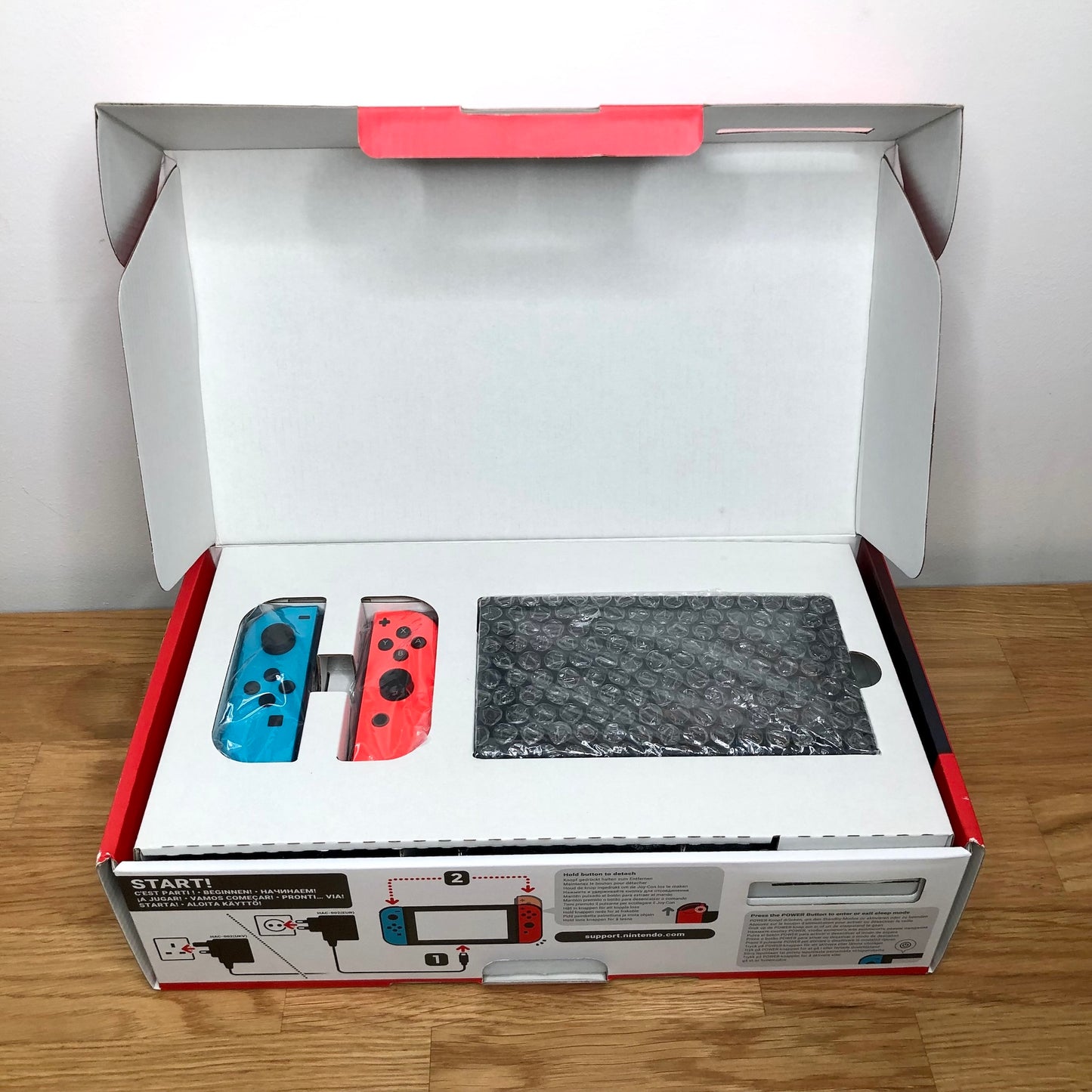 Nintendo Switch console in original box with lid open, showing console and red and blue Joy-Cons packed in top tray.