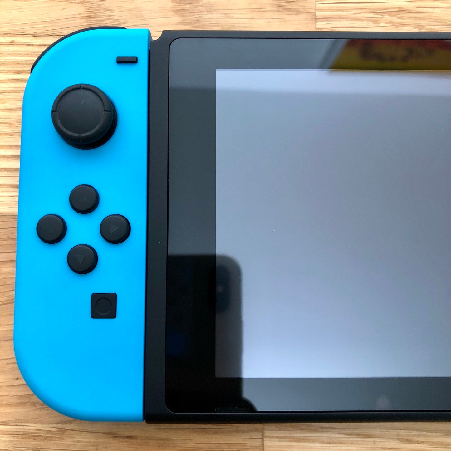 Close-up of neon blue left Joy-Con on Nintendo Switch, showing D-pad style buttons, stick and capture button.