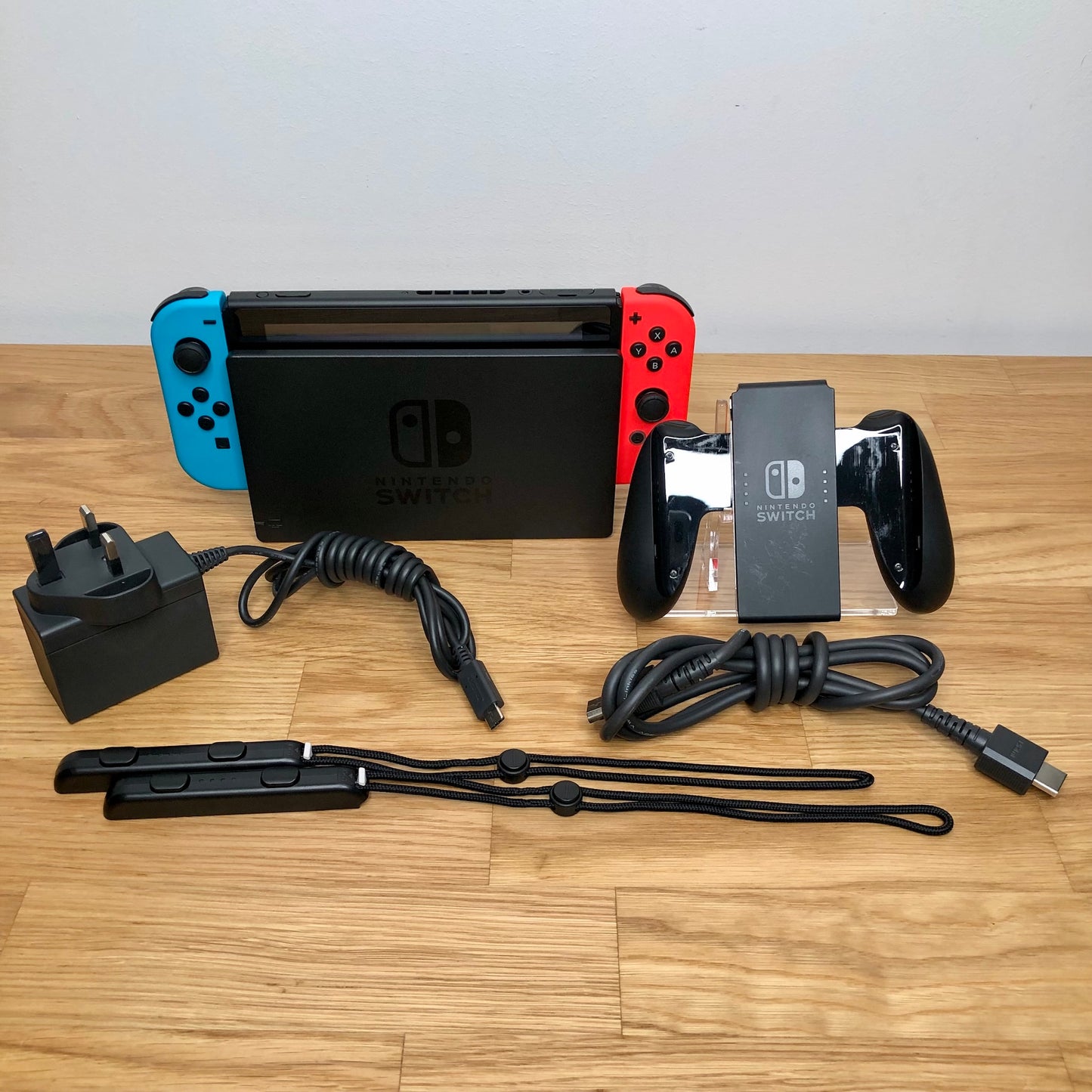 Nintendo Switch console with charger, HDMI cable, Joy-Con grip and wrist straps laid out on table.