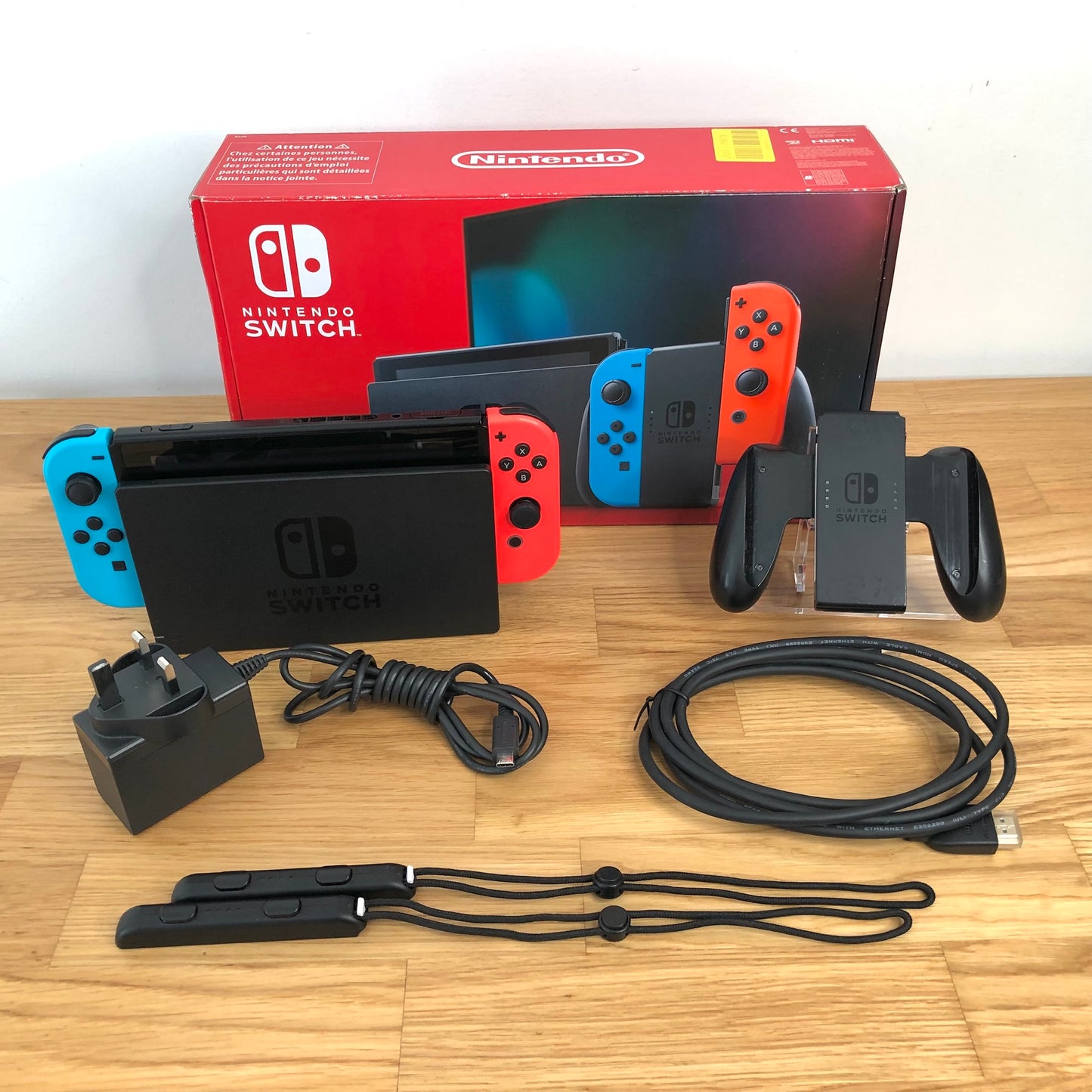 Nintendo Switch console with original box, Joy-Con grip, charger, HDMI cable and wrist straps shown.