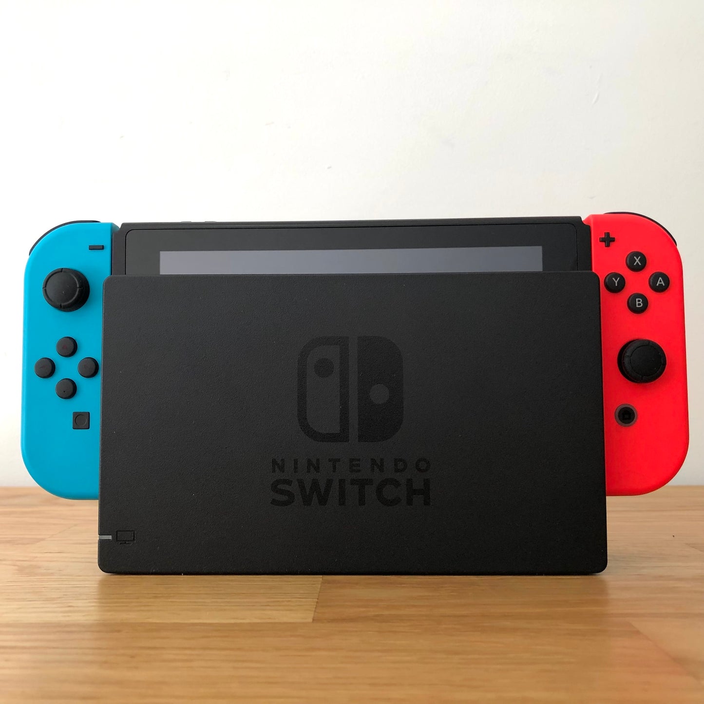 Front of Nintendo Switch console docked with red and blue Joy-Cons, showing screen edge and front buttons.