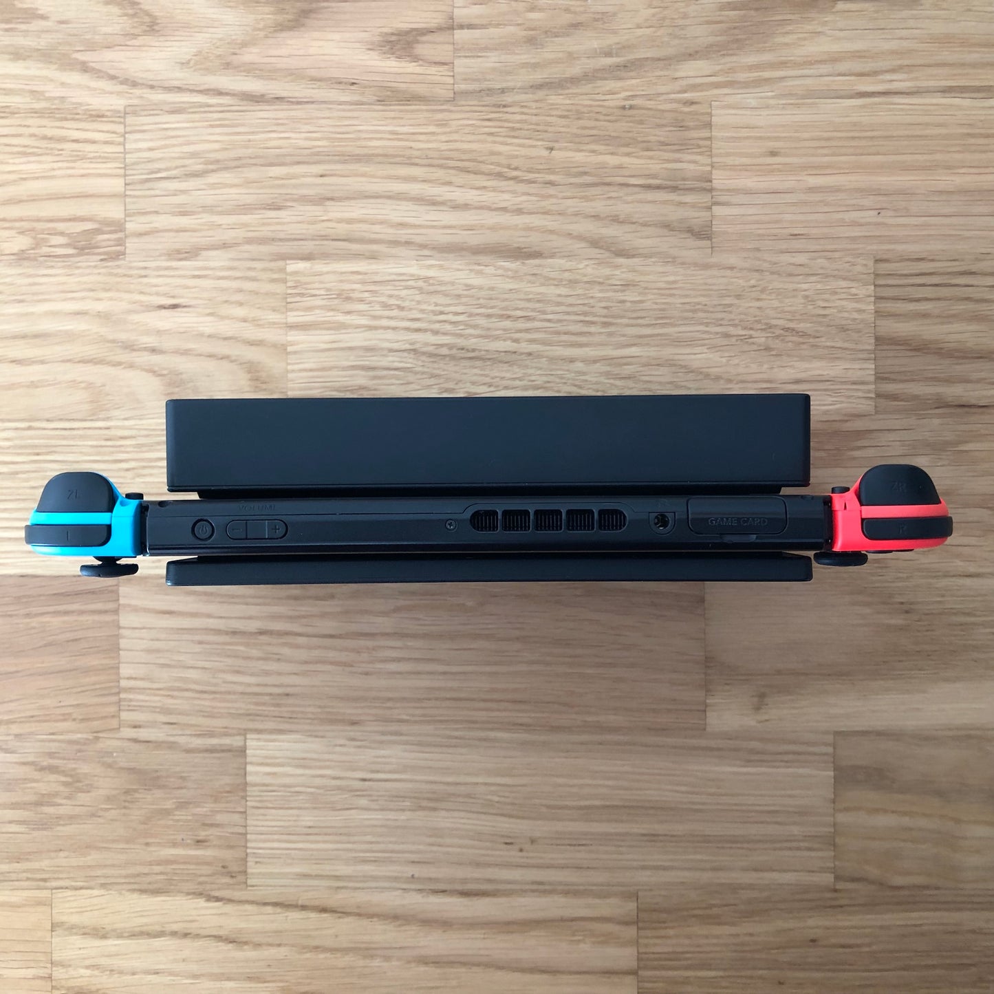 Top-down view of Nintendo Switch in dock with red and blue Joy-Cons, showing triggers, game card slot and volume buttons.