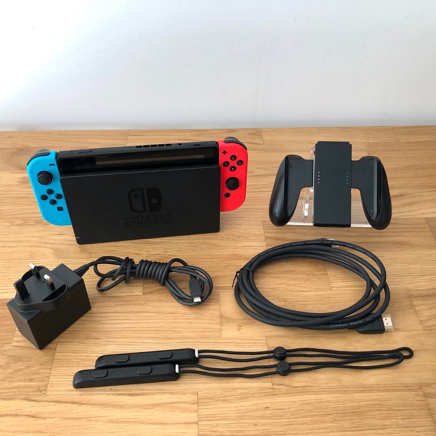 Nintendo Switch console with charger, HDMI cable, Joy-Con grip and wrist straps laid out on table.