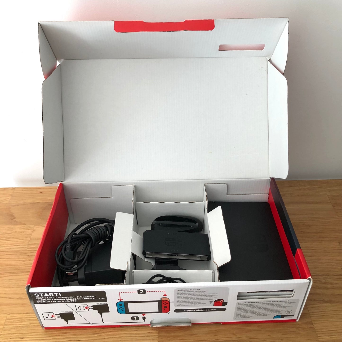 Second layer of Nintendo Switch box showing dock, Joy-Con grip, HDMI cable, charger and straps securely packed.