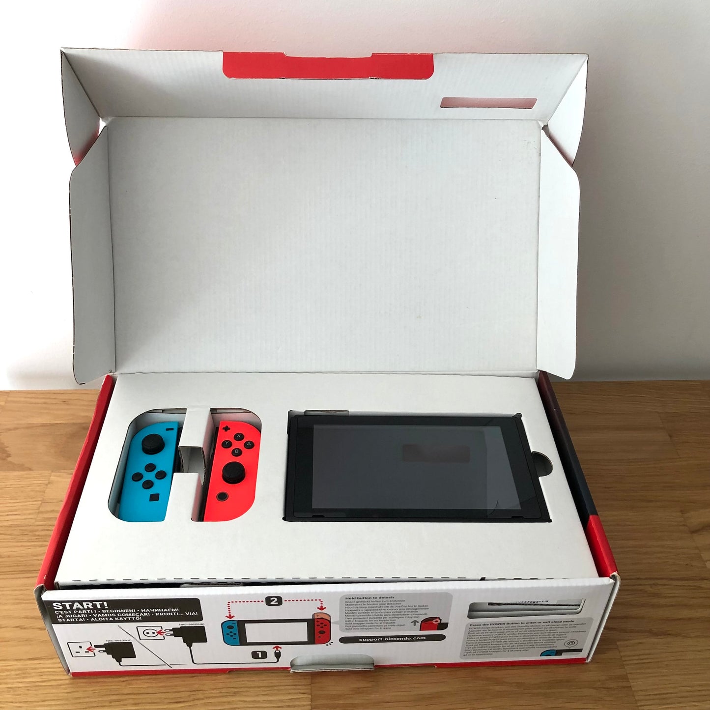 Nintendo Switch console in original box with lid open, showing console and red and blue Joy-Cons packed in top tray.
