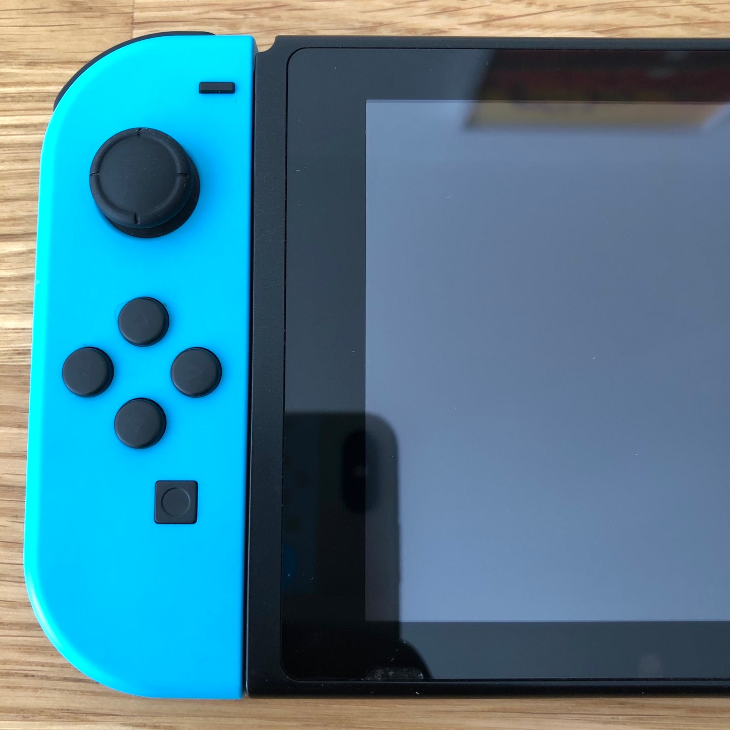 Close-up of neon blue left Joy-Con on Nintendo Switch, showing D-pad style buttons, stick and capture button.