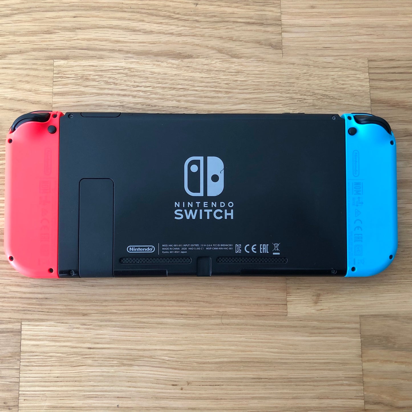 Back of Nintendo Switch console with red and blue Joy-Cons attached, showing logo, kickstand and trigger buttons laid flat.