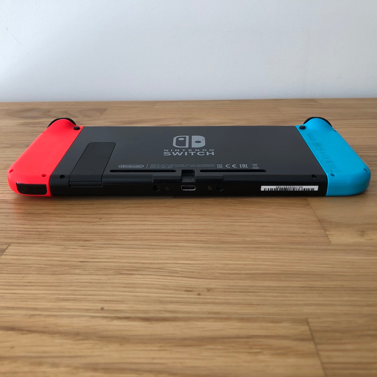 Bottom rear view of Nintendo Switch with neon Joy-Cons attached, showing logo, kickstand and microSD slot.