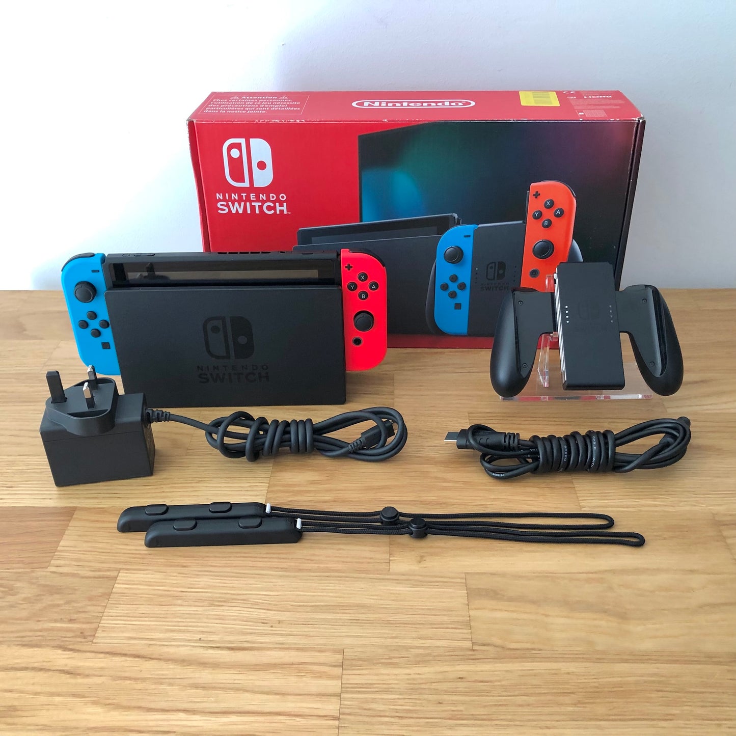 Nintendo Switch console with original box, Joy-Con grip, charger, HDMI cable and wrist straps shown.