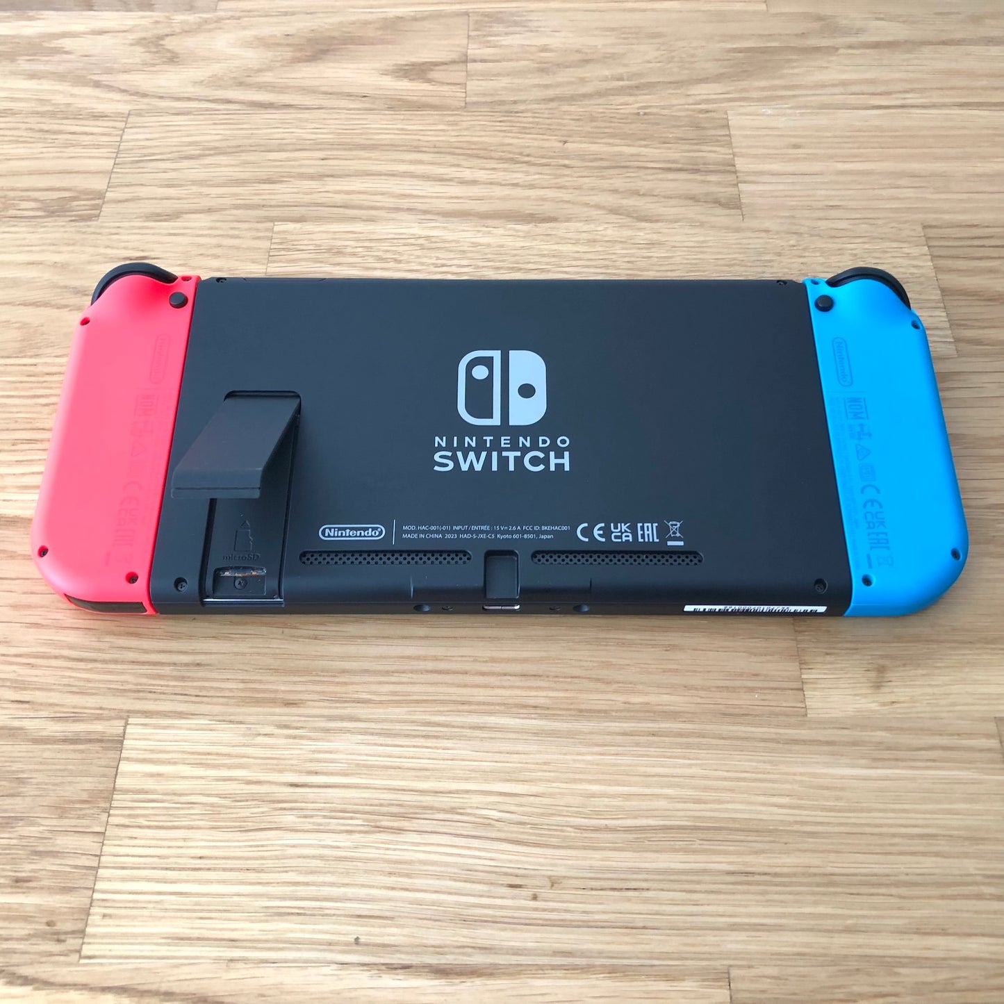 Bottom rear view of Nintendo Switch with neon Joy-Cons attached, showing logo, kickstand opened and microSD slot.