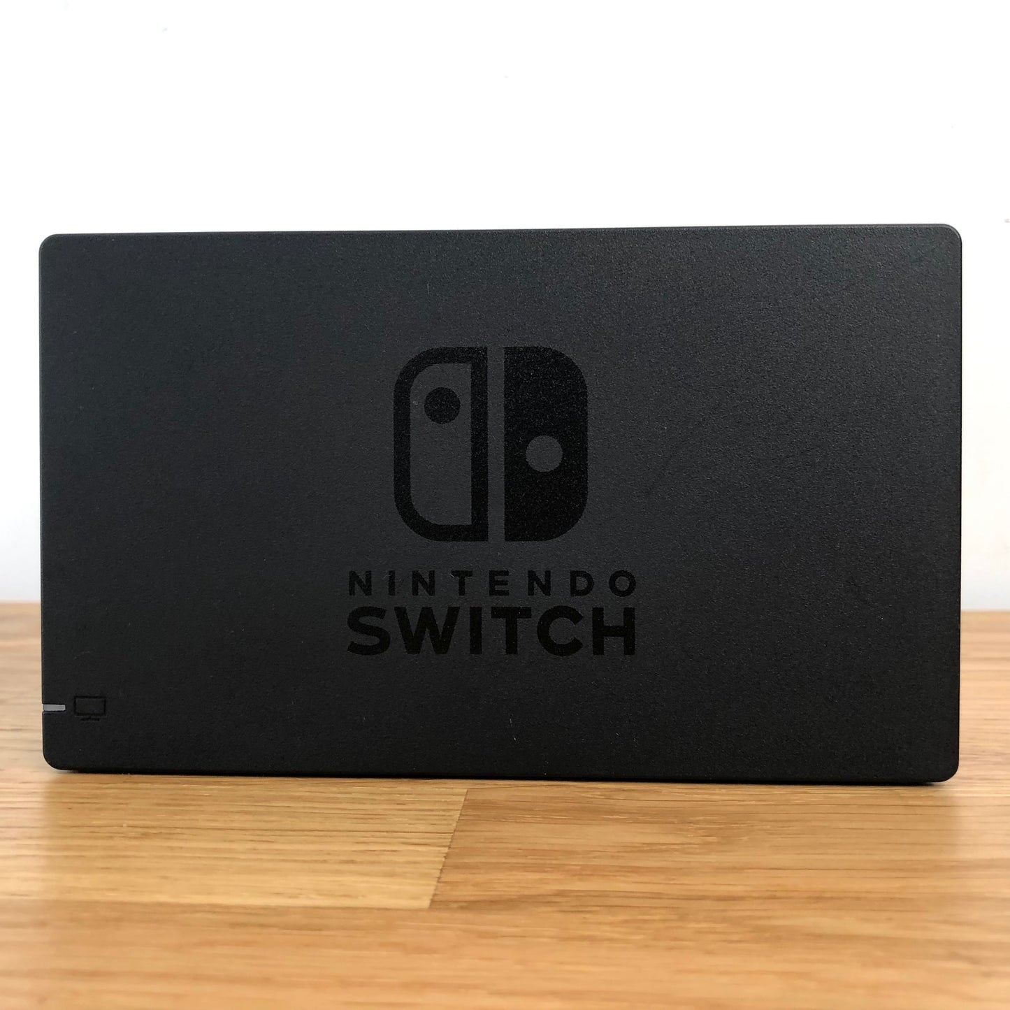 Front of Nintendo Switch dock with embossed logo, smooth matte finish and rounded edges, compatible with neon Joy-Cons.