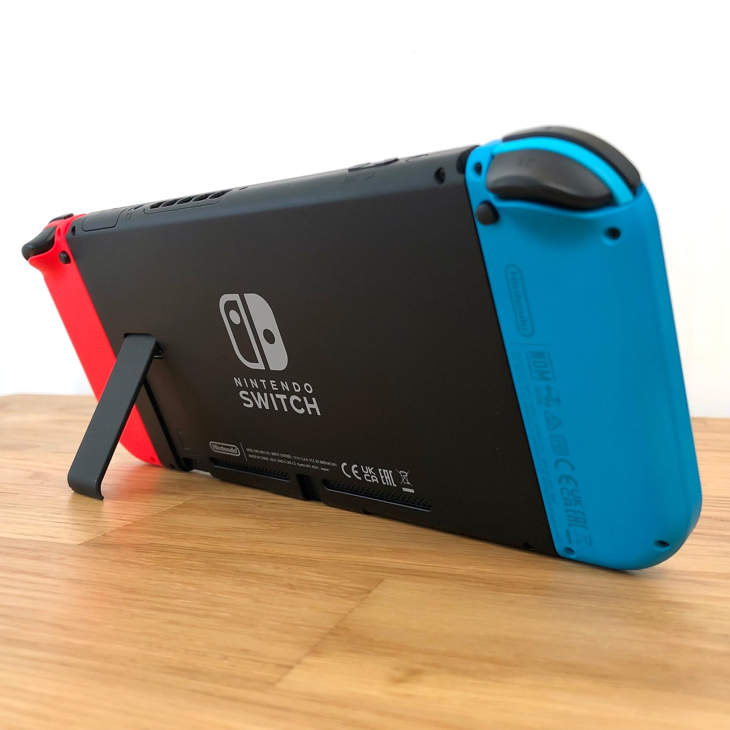 Back angled view of Nintendo Switch console with red and blue Joy-Cons attached, showing logo, kickstand and trigger buttons.