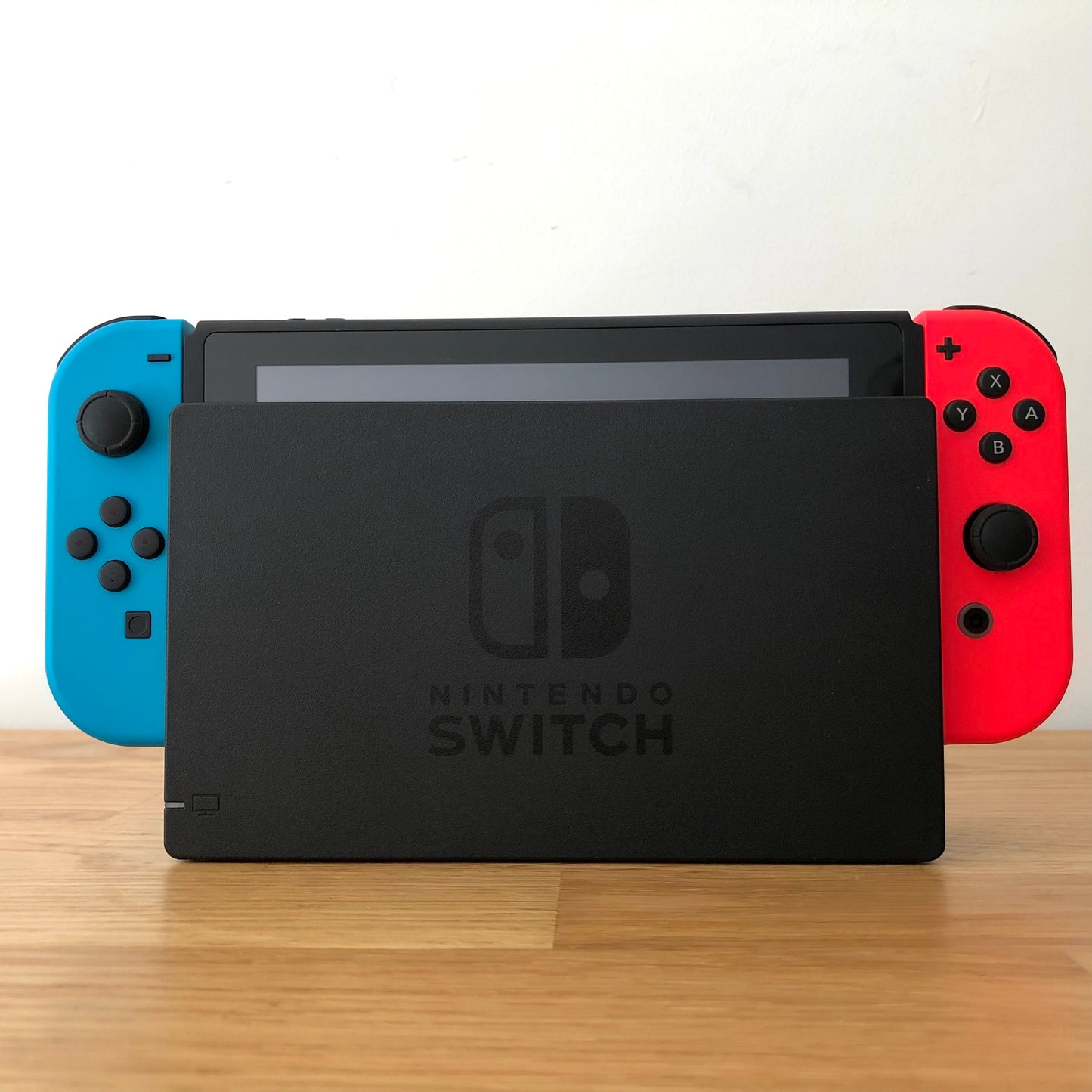 Front of Nintendo Switch console docked with red and blue Joy-Cons, showing screen edge and front buttons.