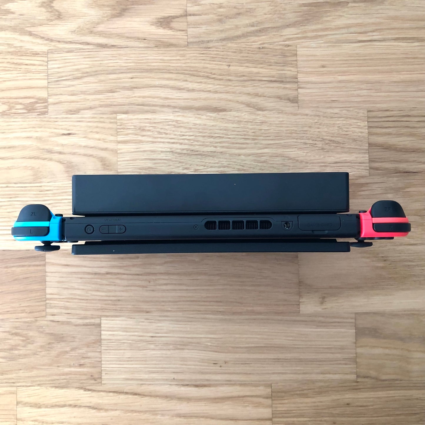 Top-down view of Nintendo Switch in dock with red and blue Joy-Cons, showing triggers, game card slot and volume buttons.