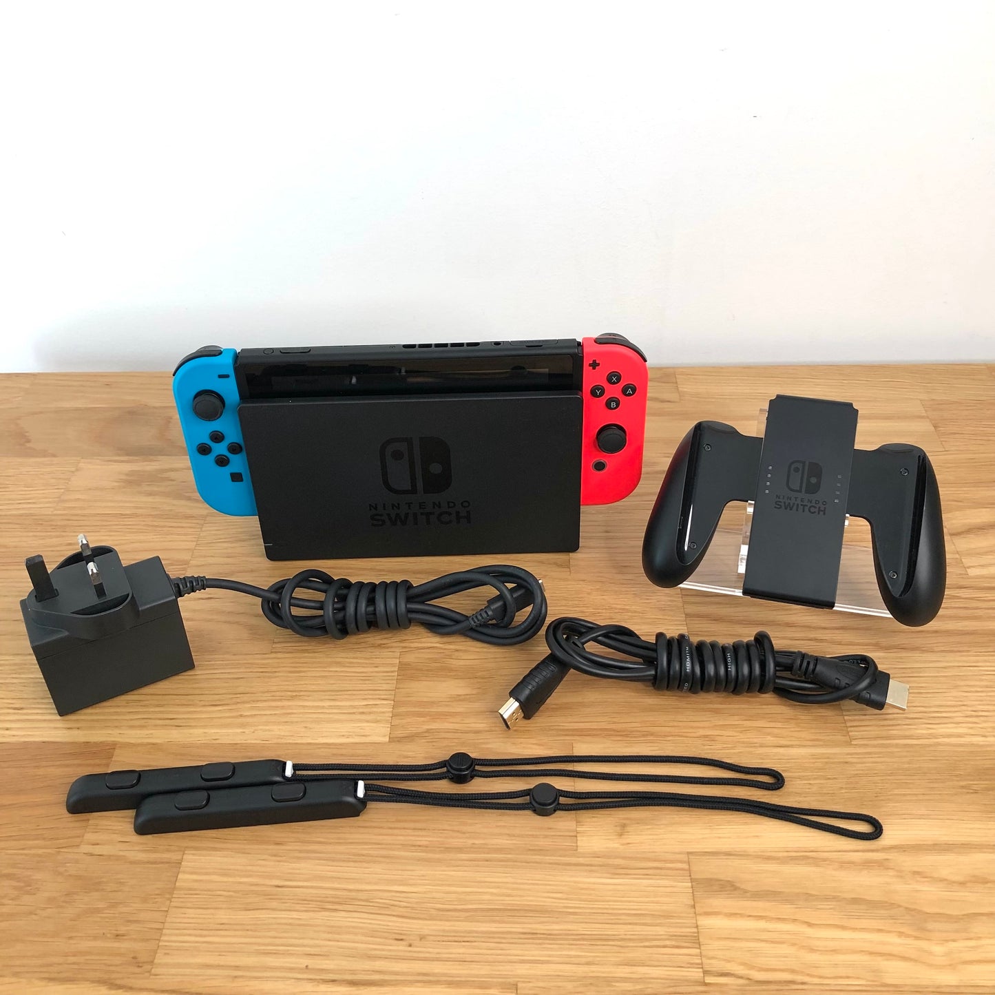 Nintendo Switch console with charger, HDMI cable, Joy-Con grip and wrist straps laid out on table.