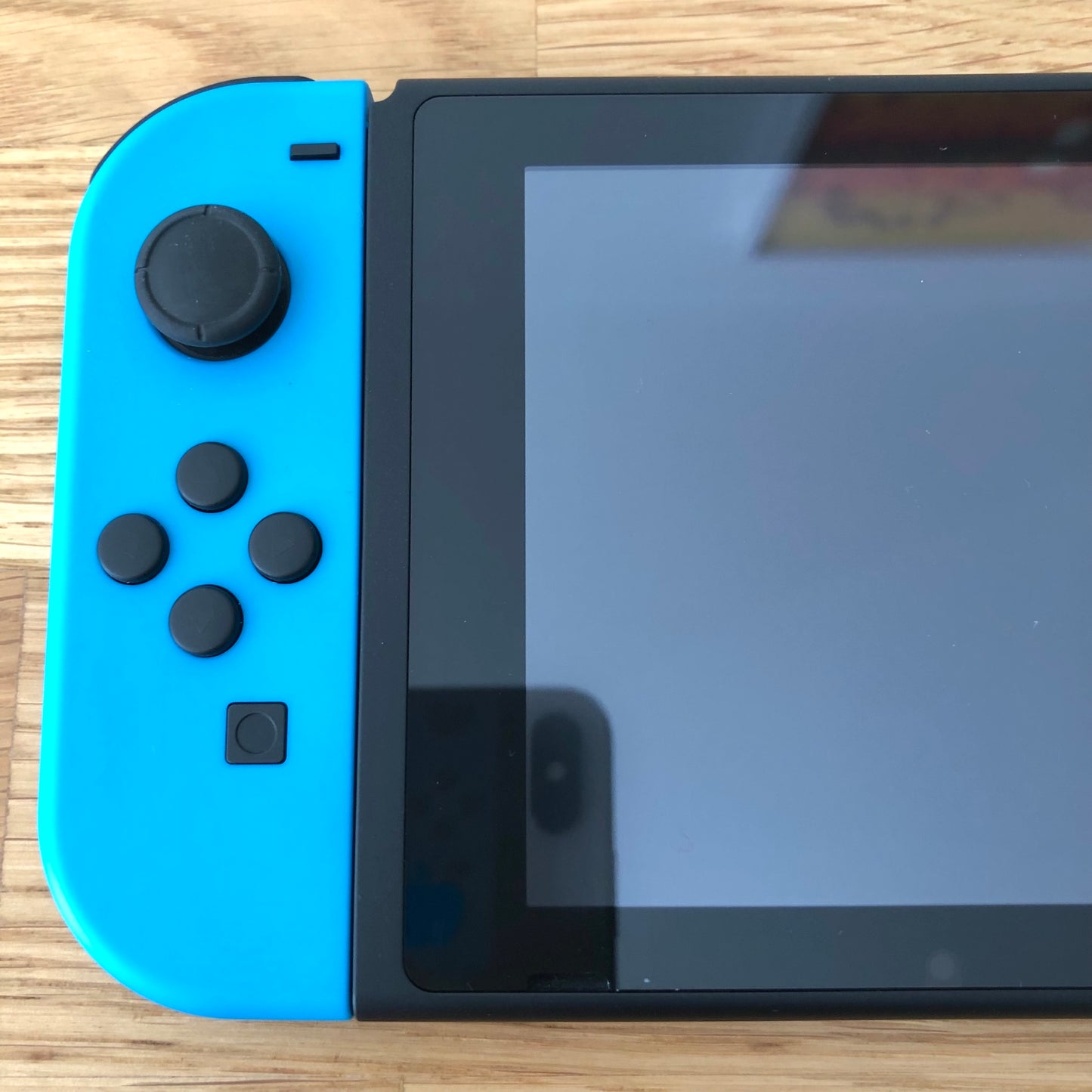 Close-up of neon blue left Joy-Con on Nintendo Switch, showing D-pad style buttons, stick and capture button.