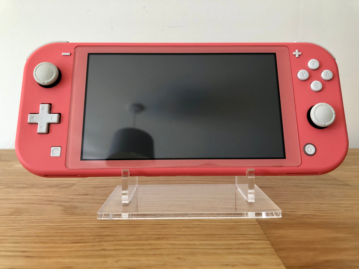 Front view of a Nintendo Switch Lite pink console, displayed on a clear acrylic stand against a light background.