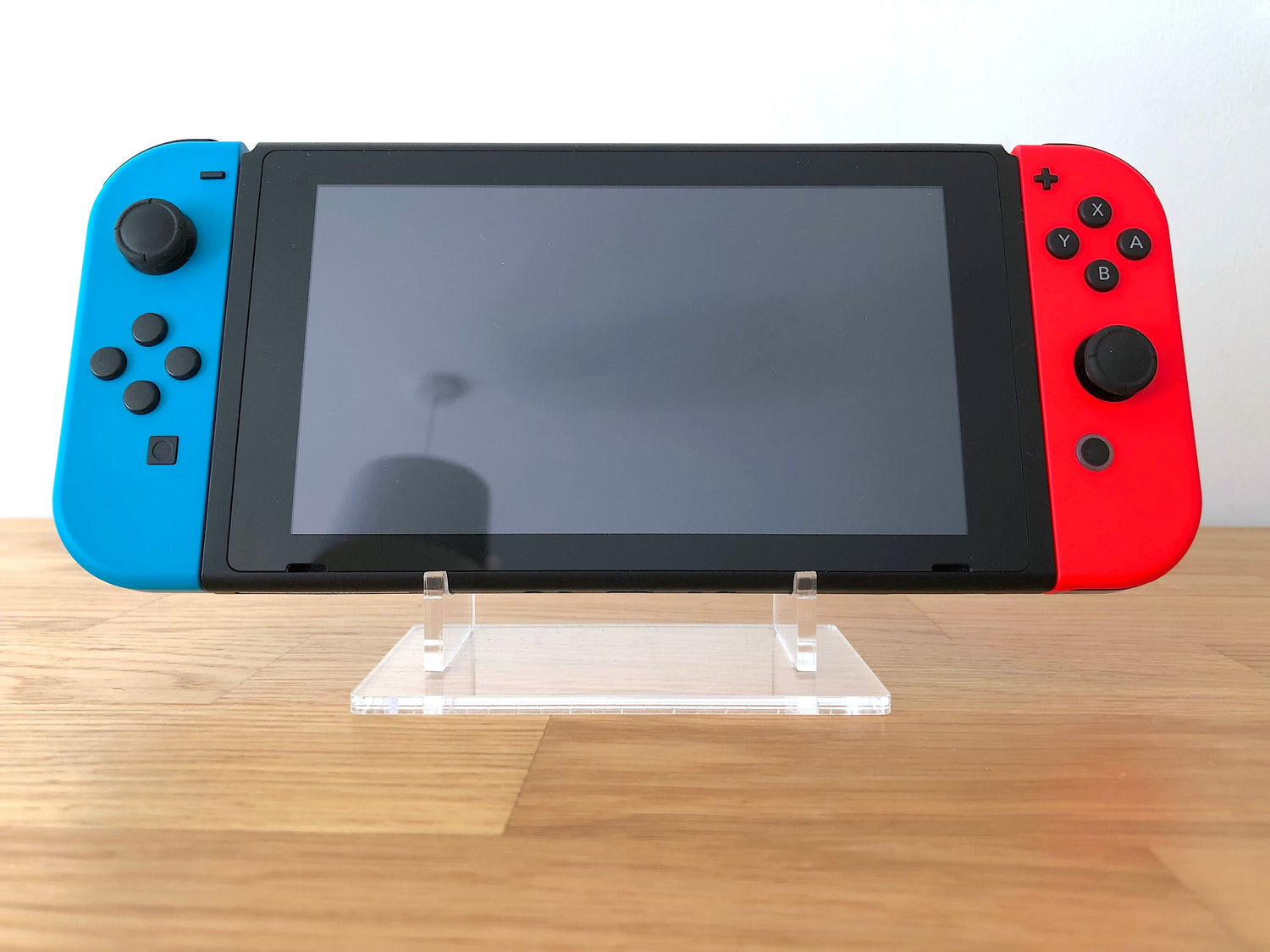 Front view of a Nintendo Switch 32GB console with Neon Blue & Red Joy-Cons, shown on a clear acrylic display stand. 