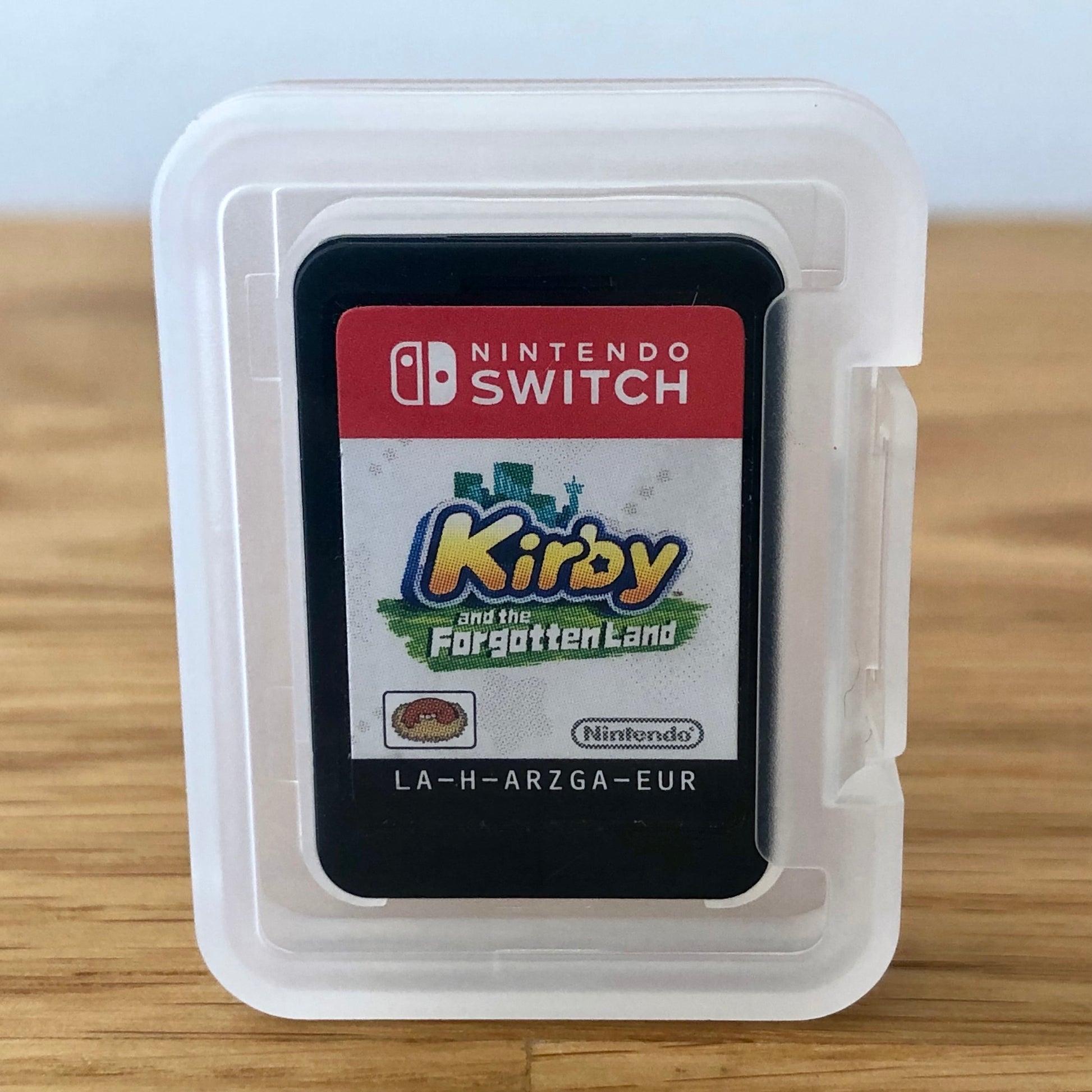 Nintendo Switch game card for 'Kirby and the Forgotten Land' in a clear plastic case on a wooden surface.