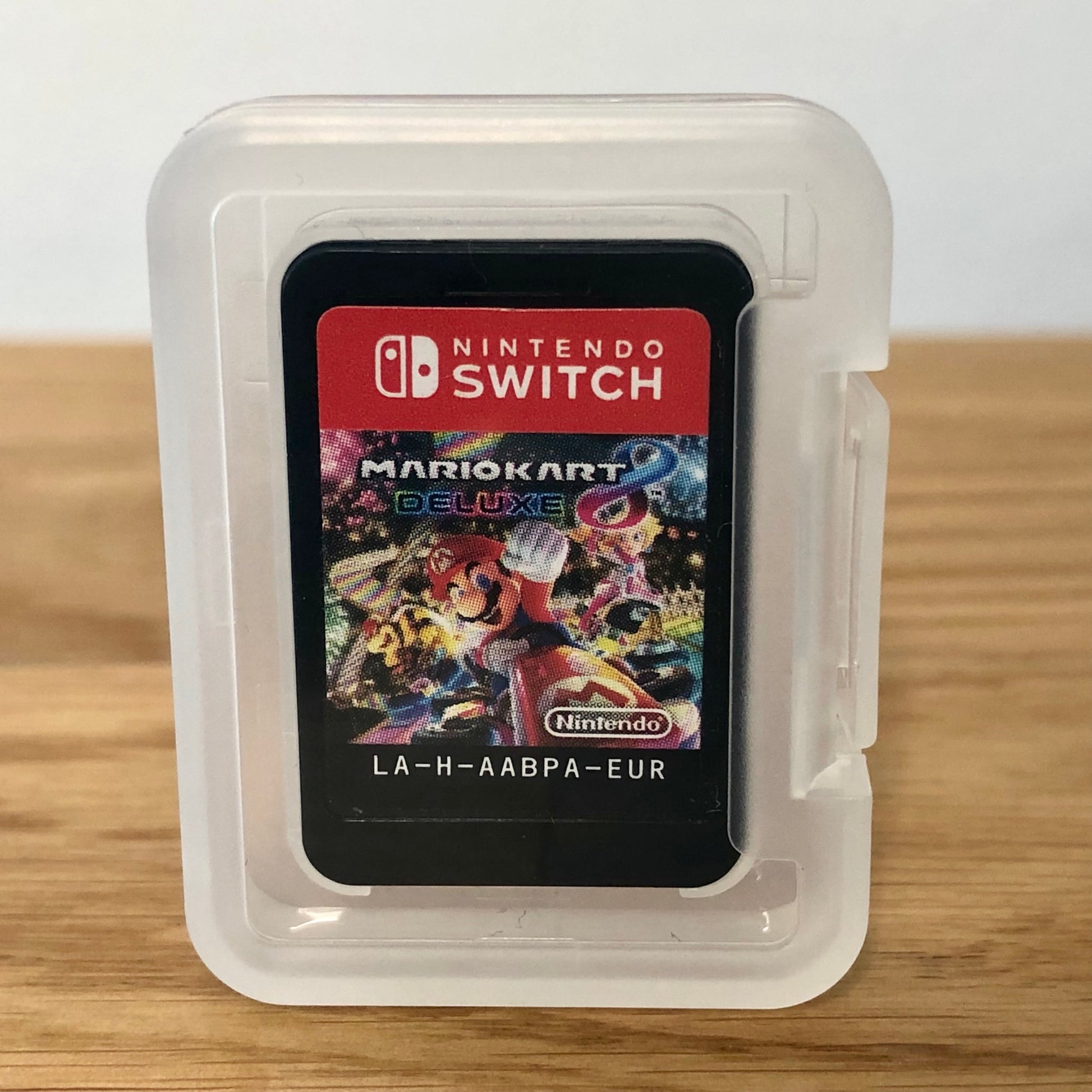 Cartridge of Mario Kart 8 Deluxe for Nintendo Switch, the cartridge is inside a cartridge size transparent protective case, through which you can see the front of the cartridge